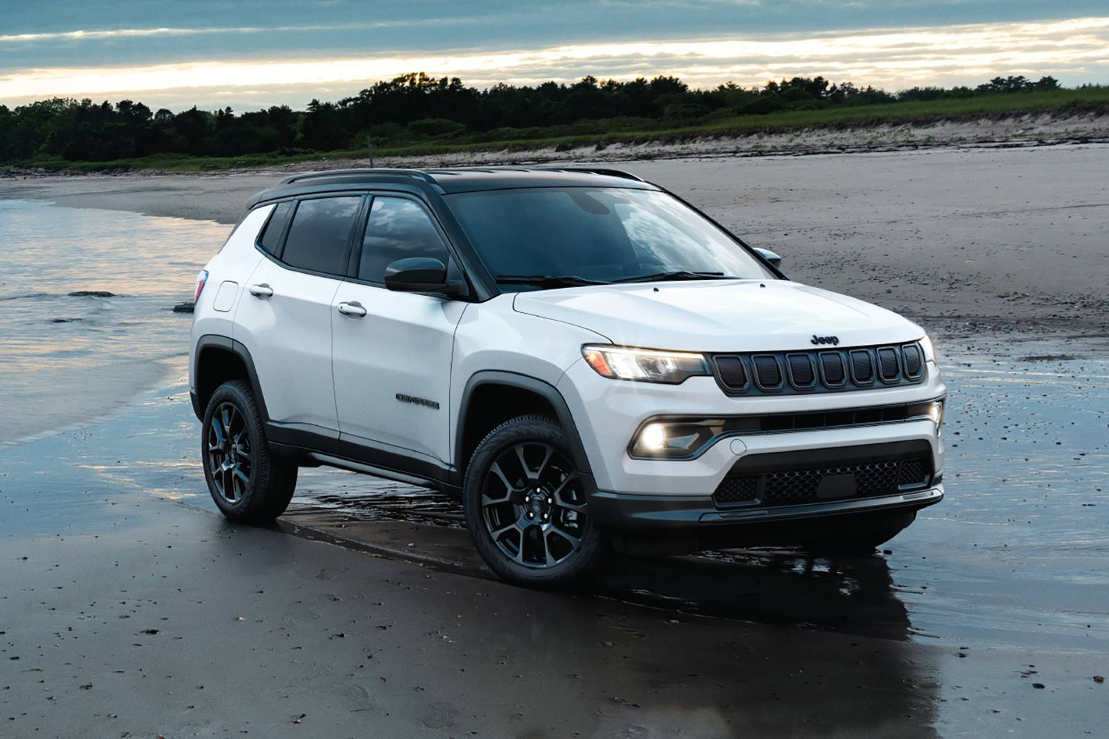 白色Jeep Compass SUV在日落時停泊在濕沙灘上