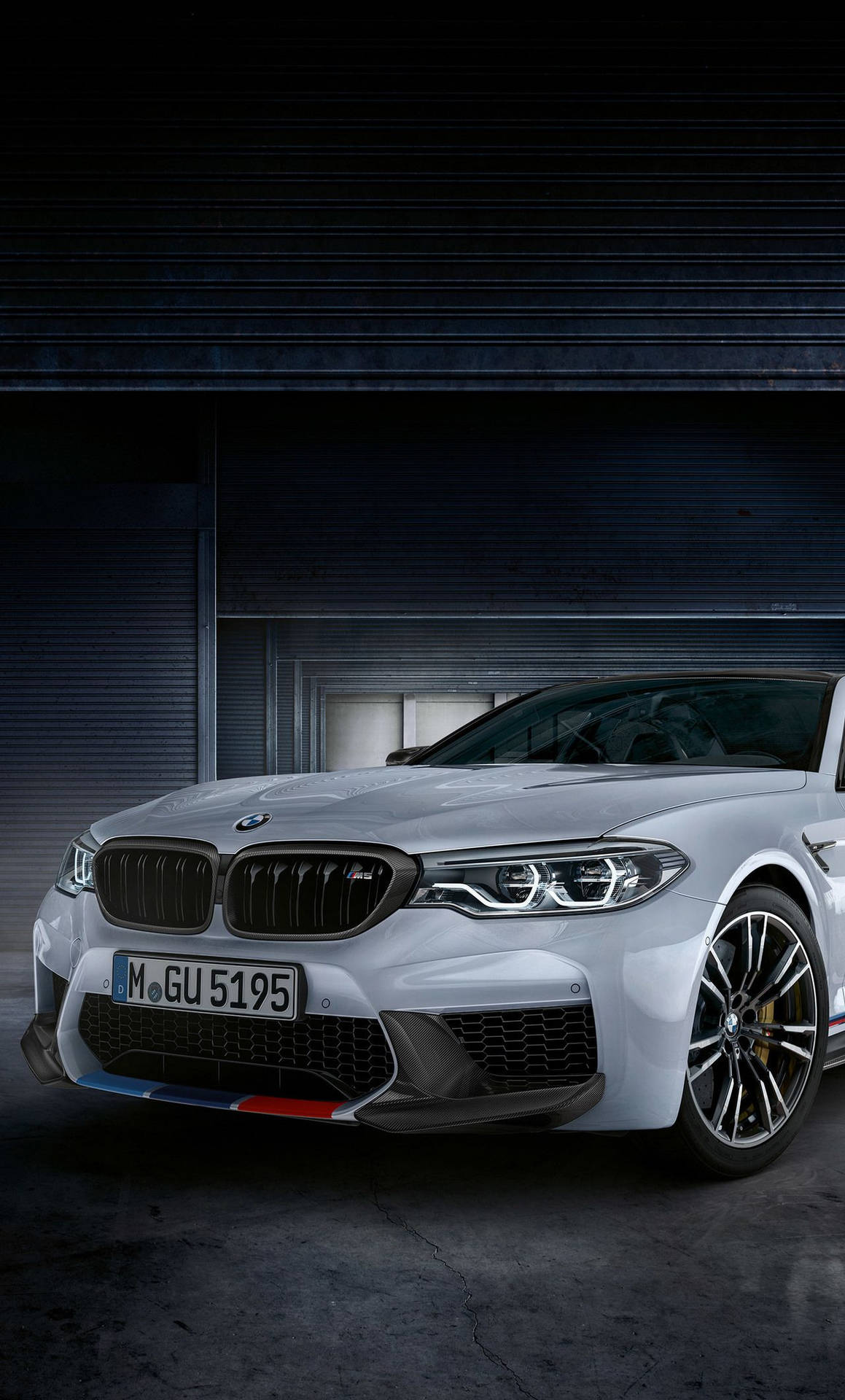 銀色BMW M5跑車停放在光線昏暗的車庫中，帶有工業捲簾門。
