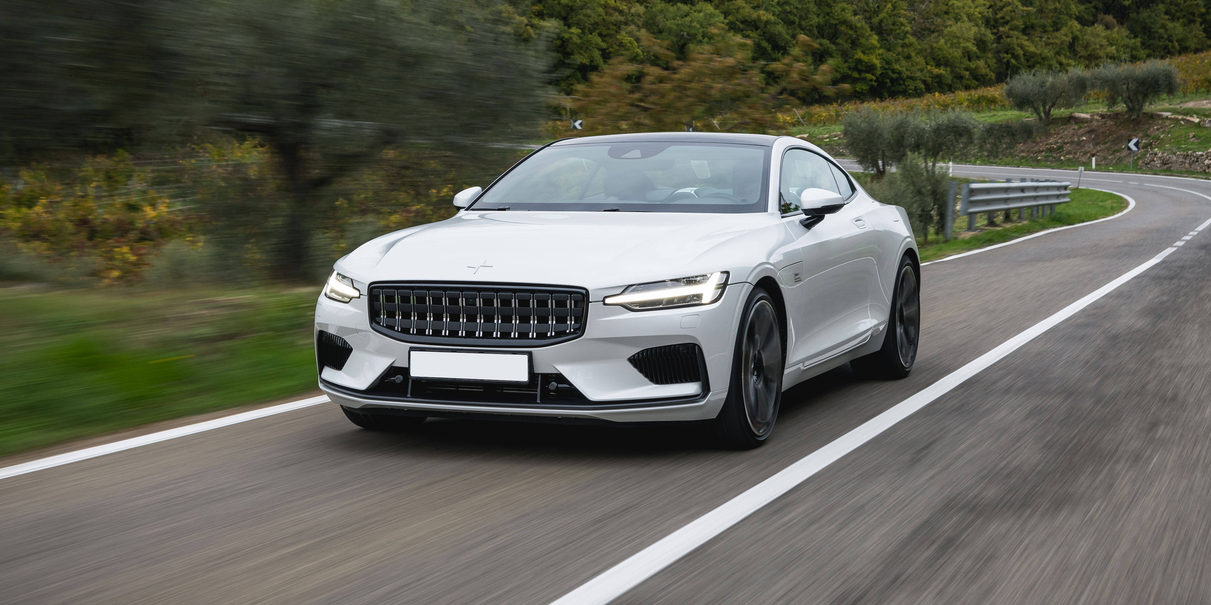 白色Polestar 1 壁紙 — 一輛時尚的白色跑車在蜿蜒的鄉村道路上飛馳，周圍環繞著茂密的綠植。