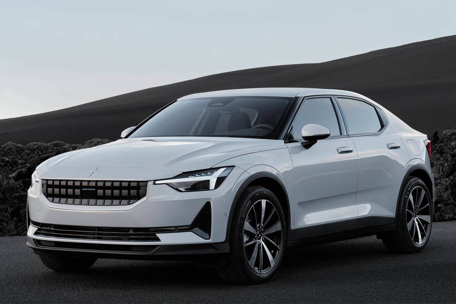 白色Polestar 2沙漠景觀 壁紙 — 一輛時尚的銀色電動車停泊在黑暗的火山地形上，背景是戲劇性的黑色山丘。