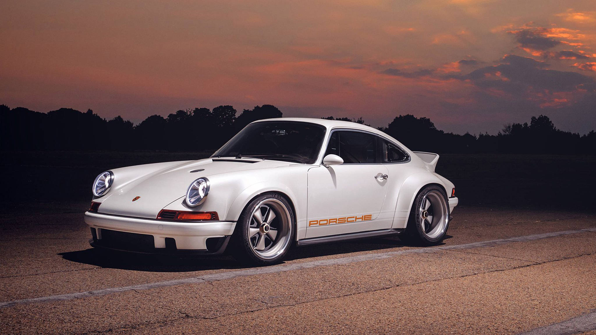 白色Singer Porsche 911 壁紙 — 一架純白色的保時捷911經典跑車停泊在瀝青路上，背景是熾熱的日落天空。