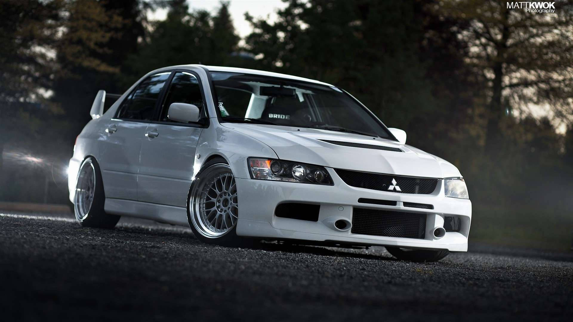 白色三菱Lancer Evolution在黃昏的樹林道路上飄移。