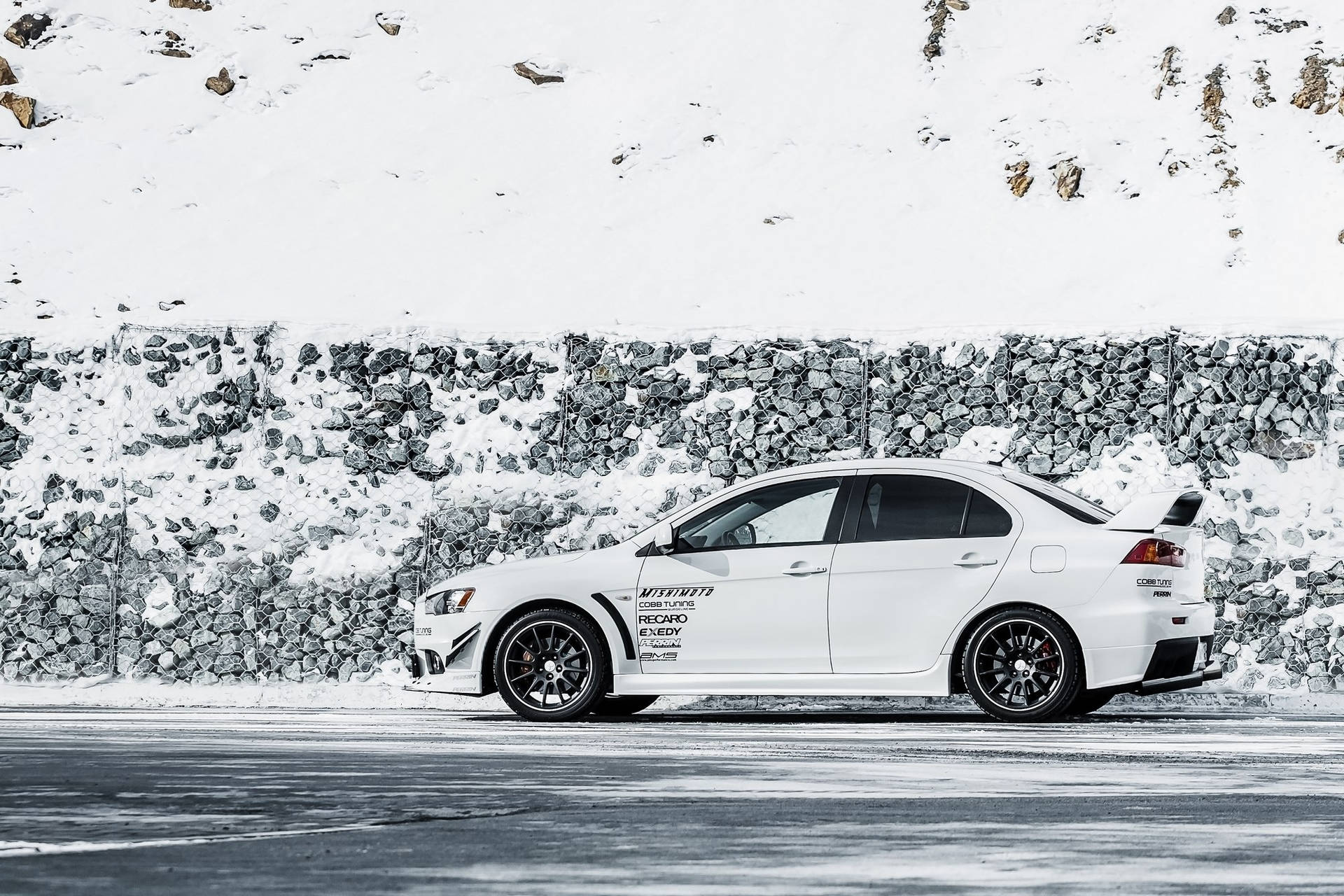 白色跑車停泊在雪路旁近石牆