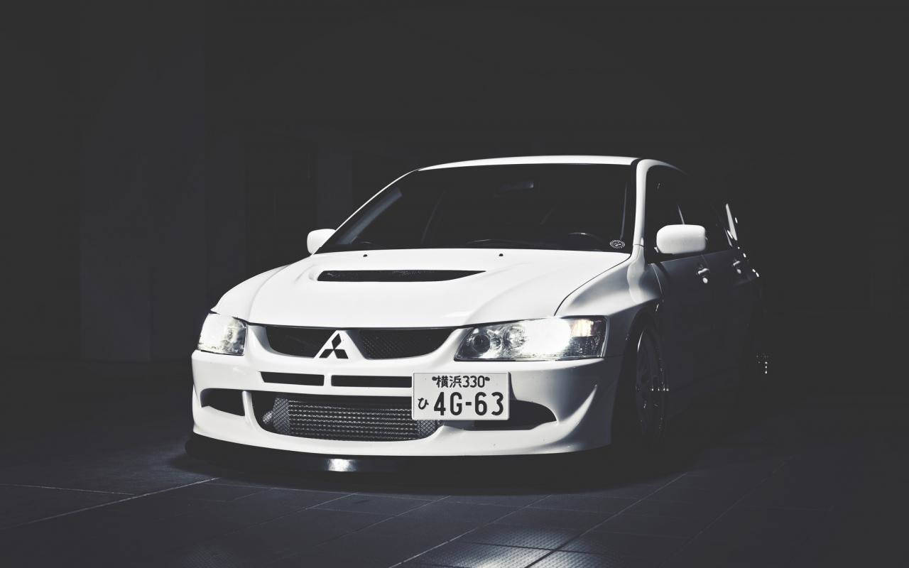白色三菱Lancer Evolution在黑暗的攝影棚中，有聚光燈。
