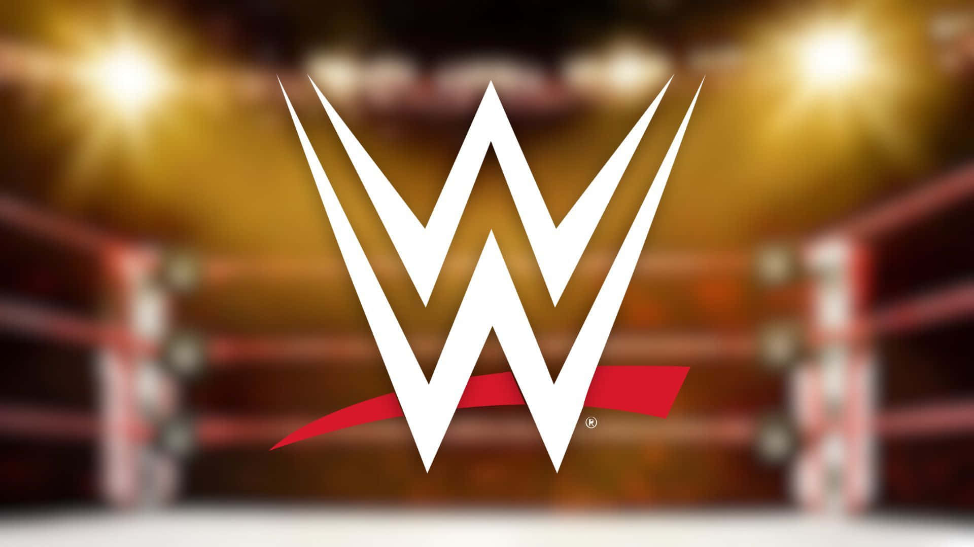 WWE Logo 桌布 壁紙 — 白色和紅色的WWE標誌在明亮的場館燈光下主導著模糊的摔角擂台。