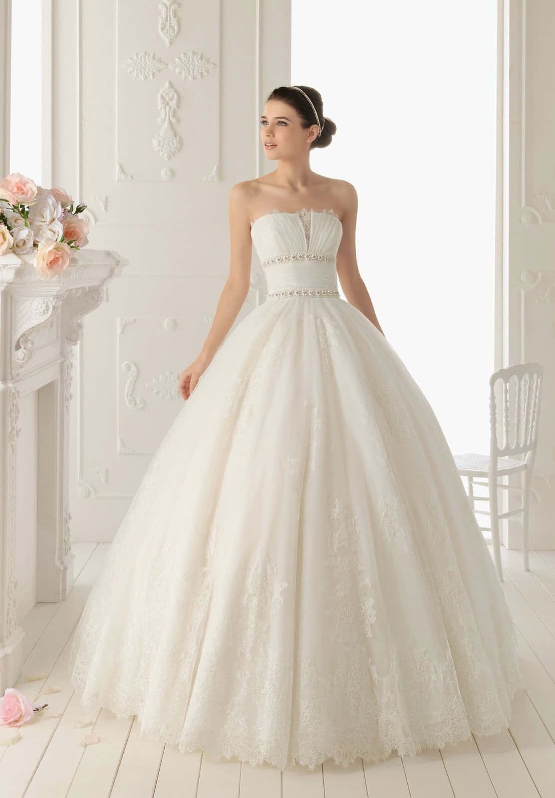 白色婚紗的特寫 壁紙 — 一位新娘穿著寬大的白色蕾絲婚紗，優雅地站在一個明亮華麗、帶有花卉裝飾的白色房間裡。