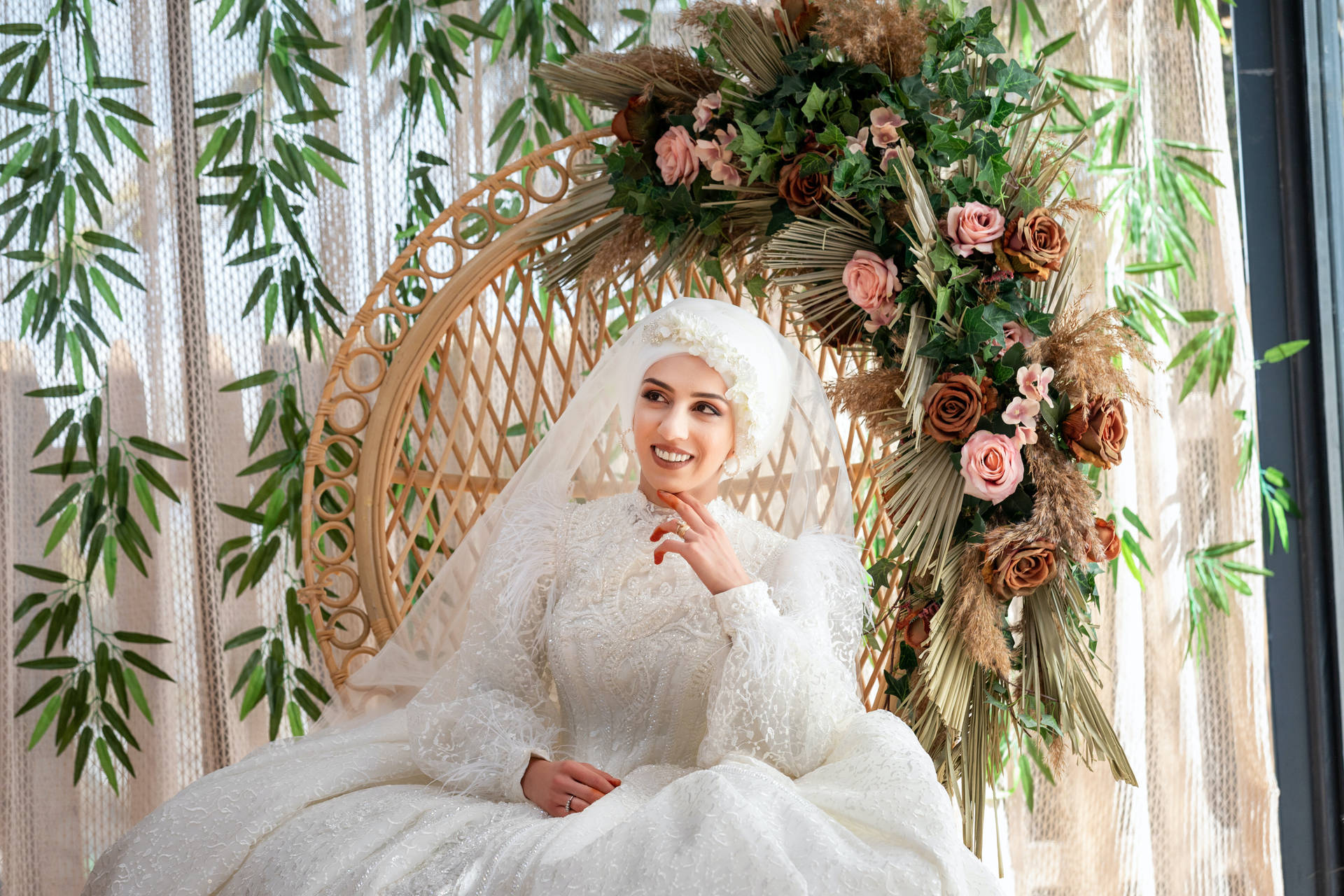 一位微笑的新娘身穿白色蕾絲婚紗，坐在裝飾過的柳條椅上。