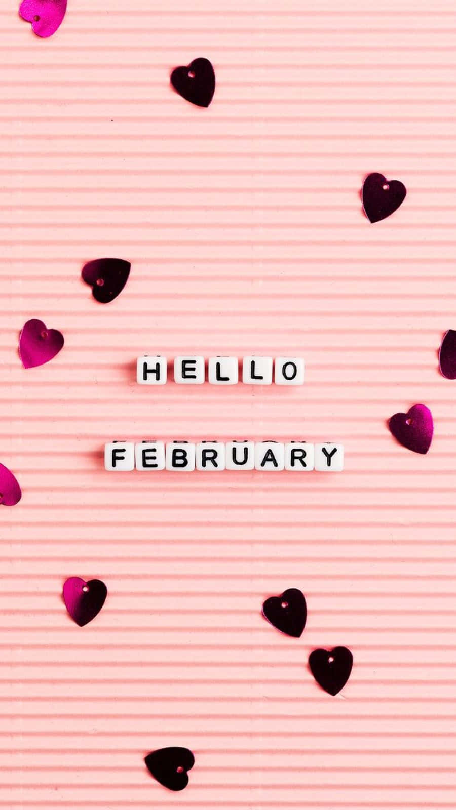 February iPhone 桌布 壁紙 — 白色字母瓷磚在粉紅色波紋表面上拼出 hello february，周圍散落著深粉紅色心形。
