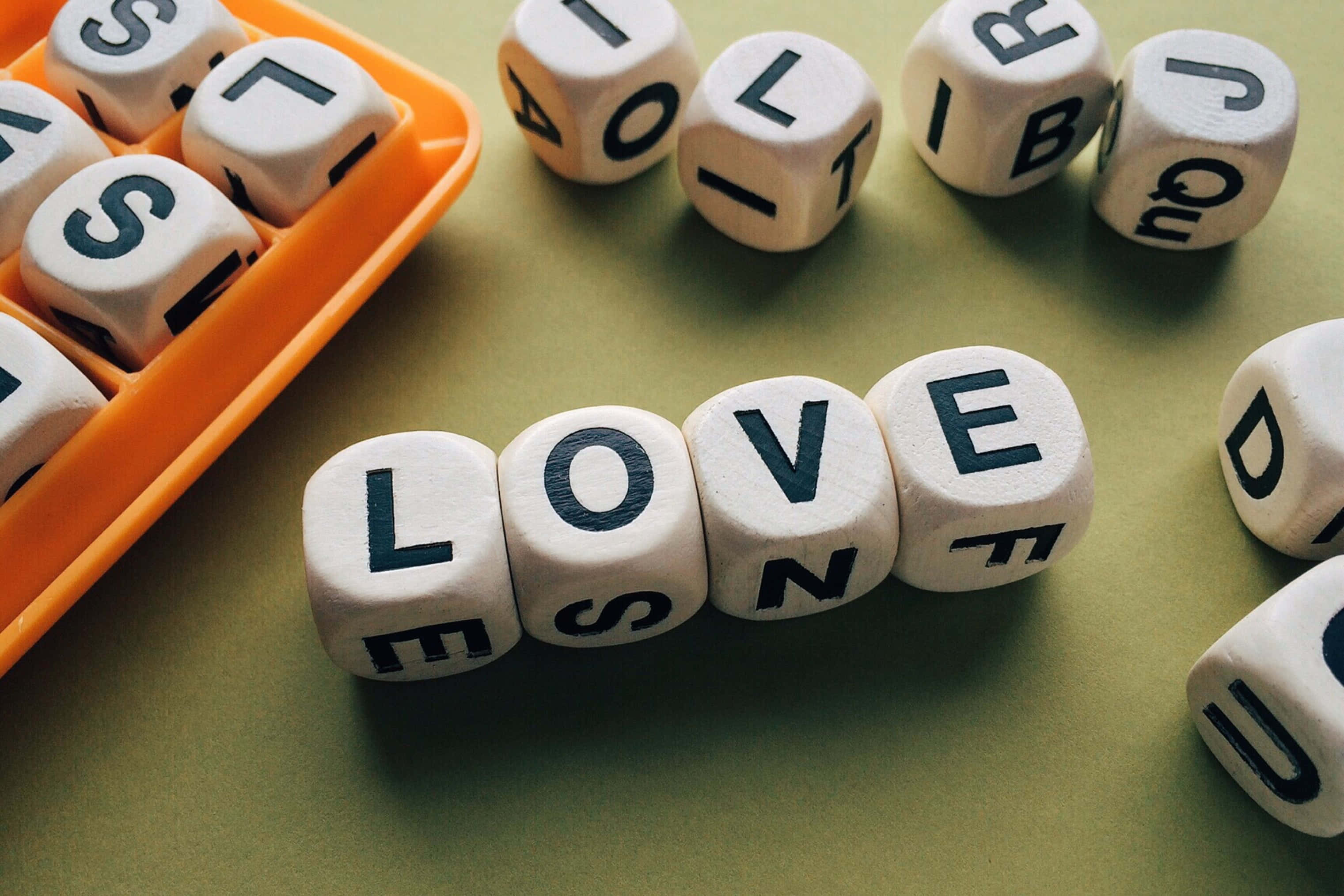 Educational Games 桌布 壁紙 — 白色字母骰子在柔和的綠色表面上拼出 LOVE，一個橙色托盤盛放著散落的骰子。