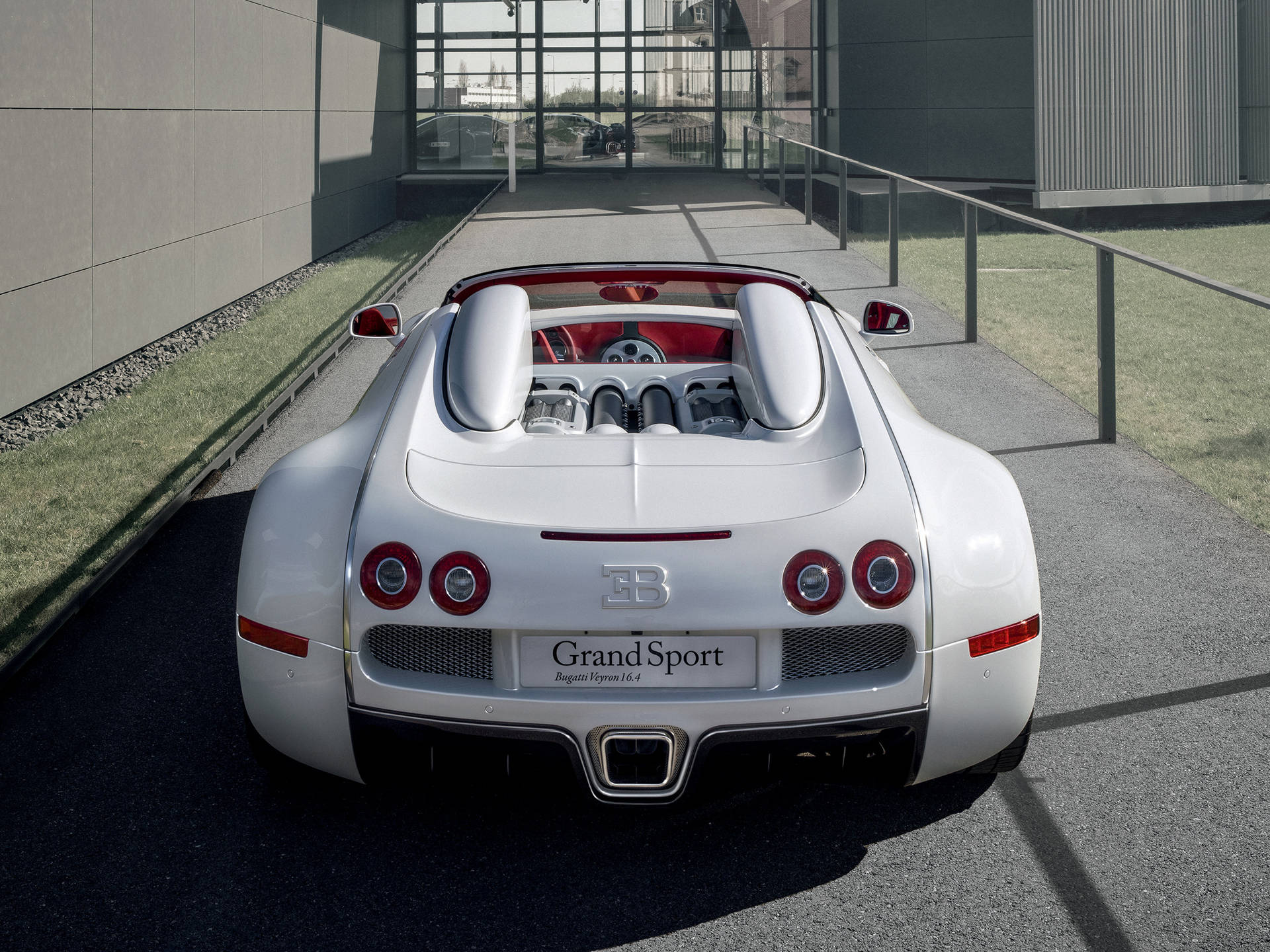 白色Bugatti Veyron Grand Sport開篷車停泊在現代玻璃建築附近。