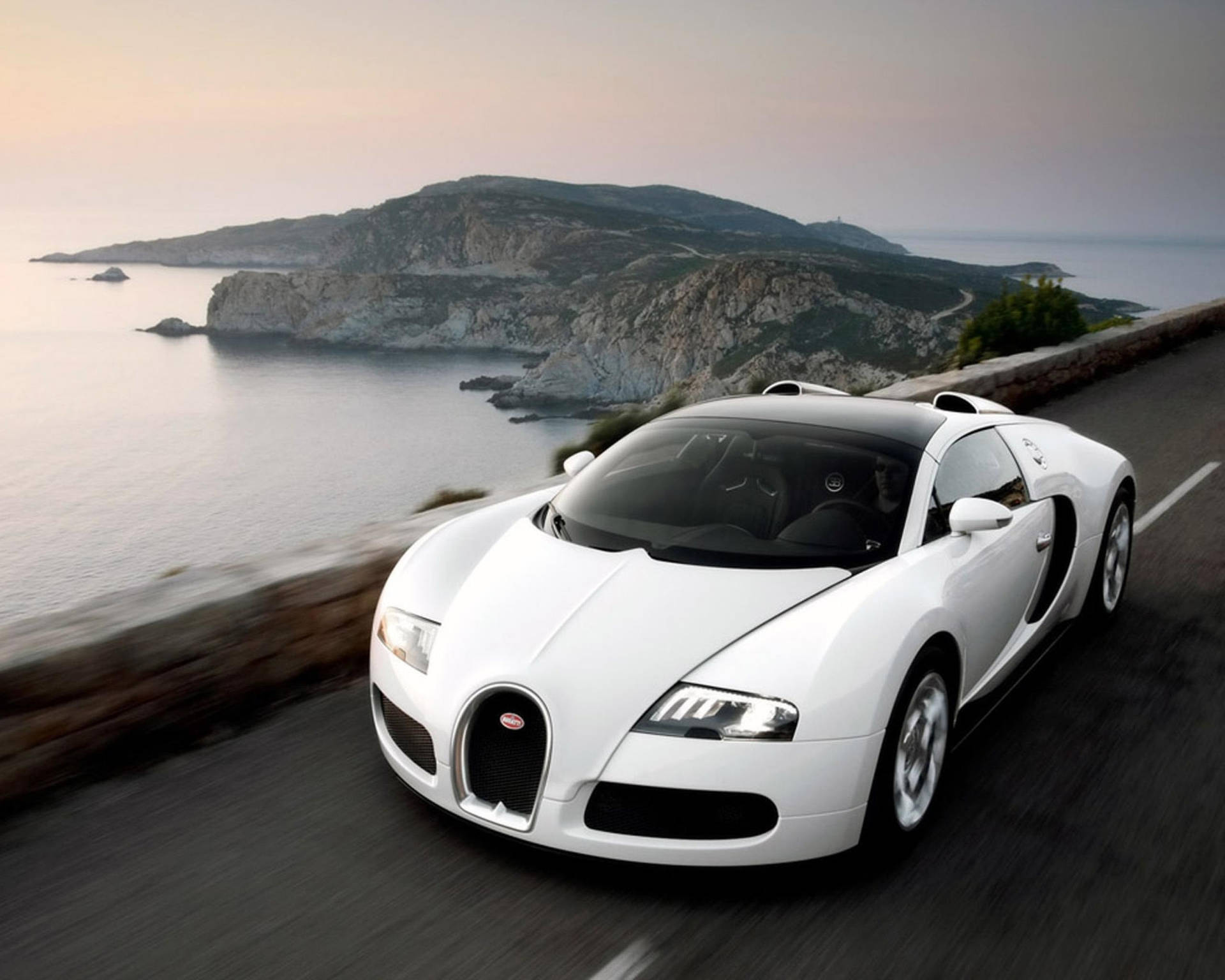 白色Bugatti Veyron在日落時分海岸公路飛馳。