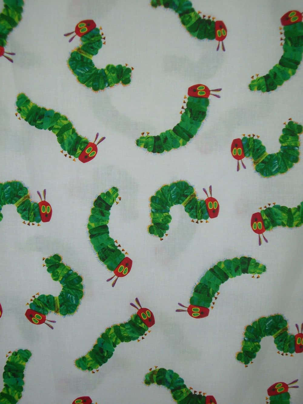 Caterpillar Transformation 桌布 壁紙 — 白色布料上重複的綠色毛蟲圖案，紅色頭部，黃色眼睛。