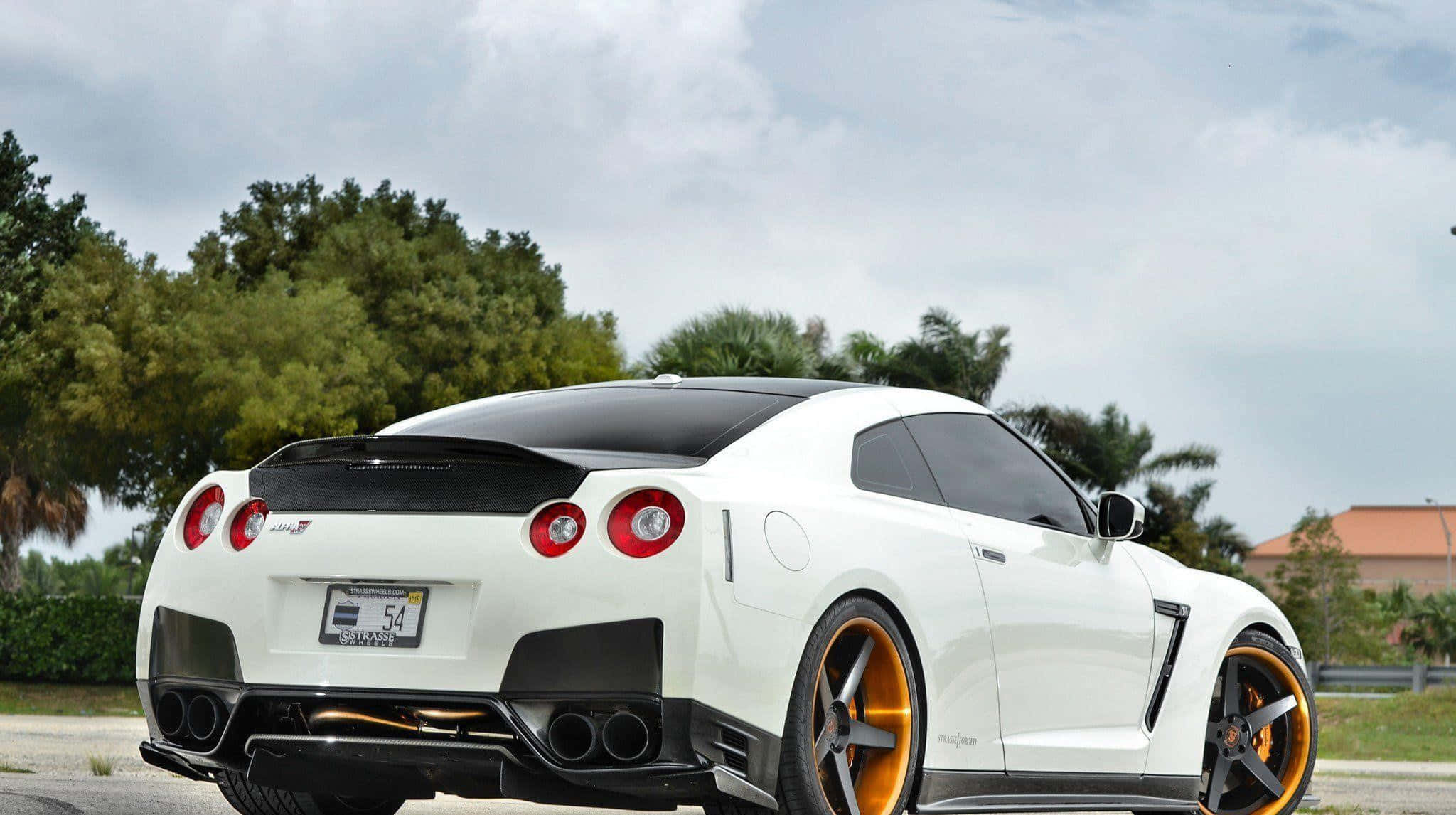 Modified Car 桌布 壁紙 — 白色日產GT-R，金色輪圈及黑色飾邊，在戶外多雲天空下，背景有棕櫚樹停泊。
