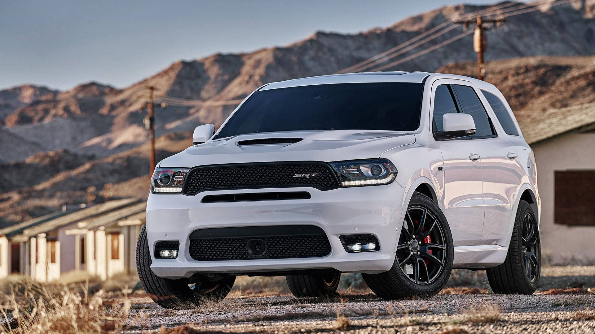 白色杜蘭戈與山景背景 壁紙 — 一輛白色Dodge Durango SRT SUV配黑色輪圈，在沙漠景觀中傲然矗立，背後有山脈和古老建築。