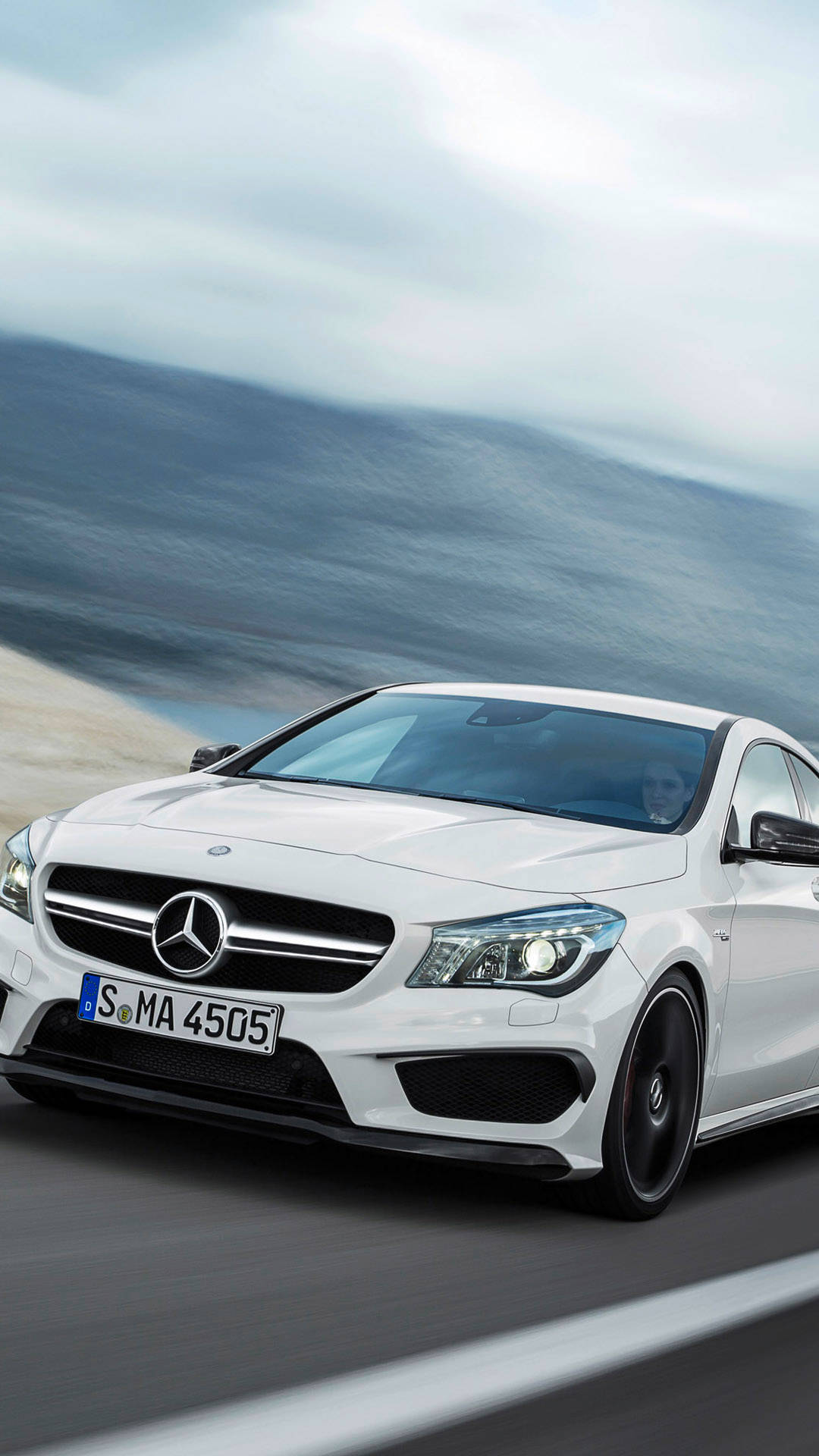 白色Mercedes跑車在日落時分於海岸公路上飛馳。