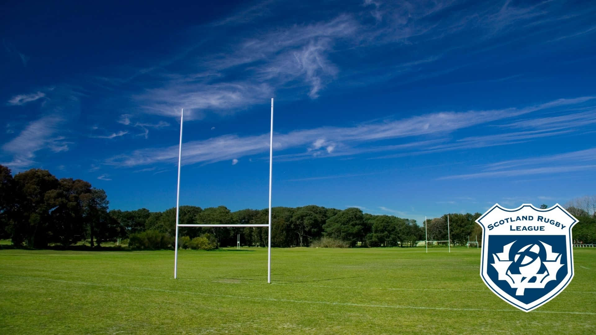 Scotland Rugby 桌布 壁紙 — 白色欖球柱在晴朗藍天和薄雲下，聳立在充滿活力的綠色球場上。