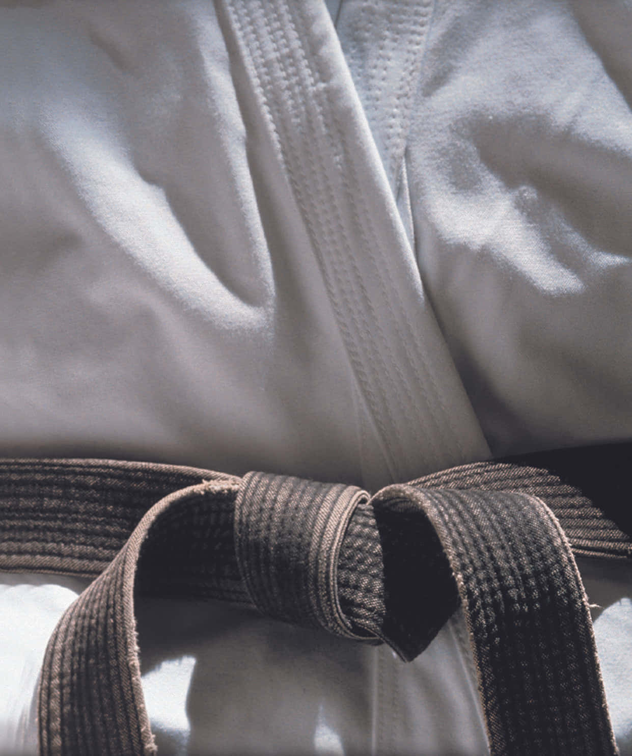 Martial Arts Uniform 桌布 壁紙 — 白色武術道服的特寫，深棕色腰帶在柔和自然光下打結。