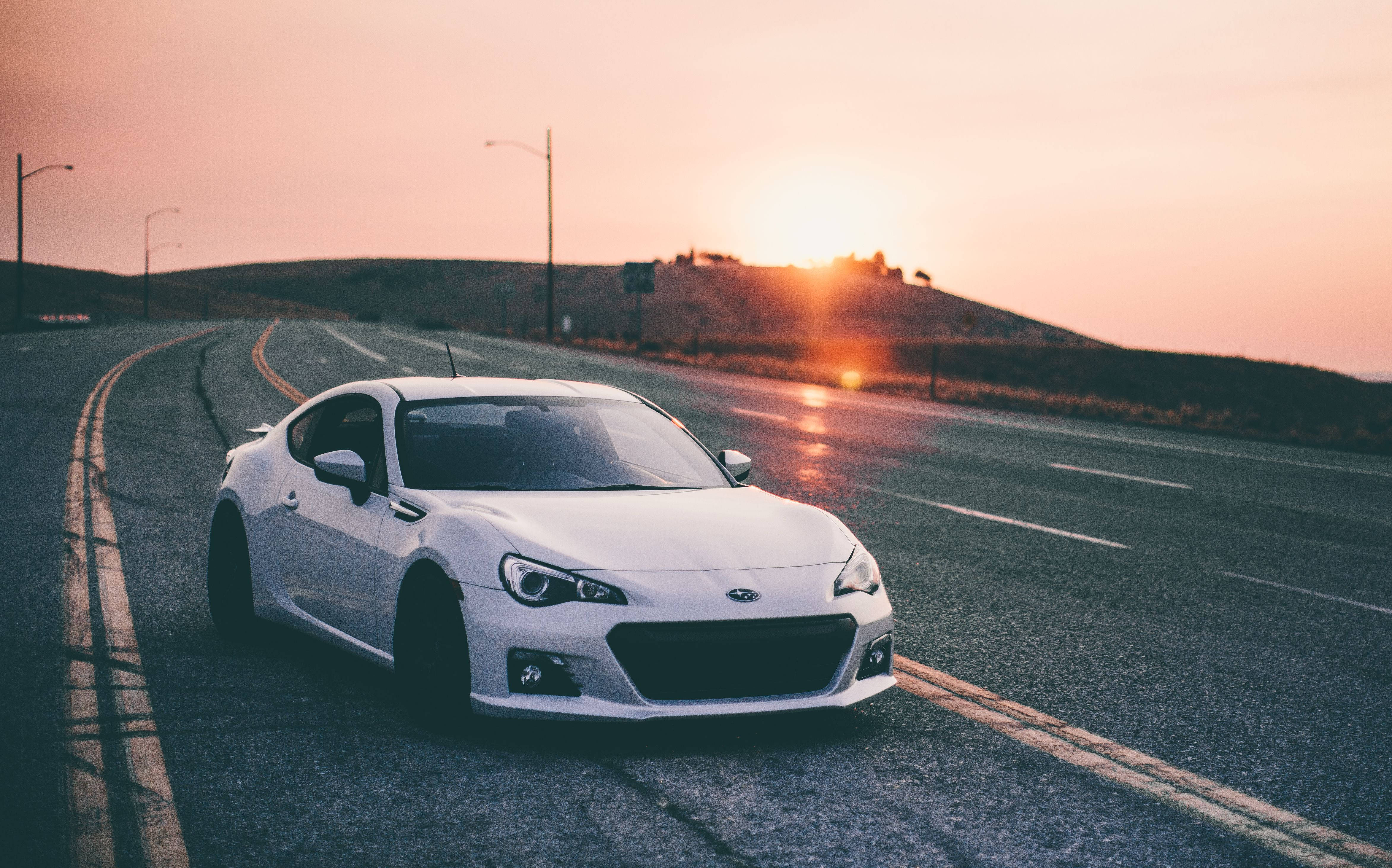 白色渦輪斯巴魯BRZ 壁紙 — 一輛白色跑車停泊在蜿蜒的道路上，夕陽落在山丘後方，灑下溫暖的光芒。