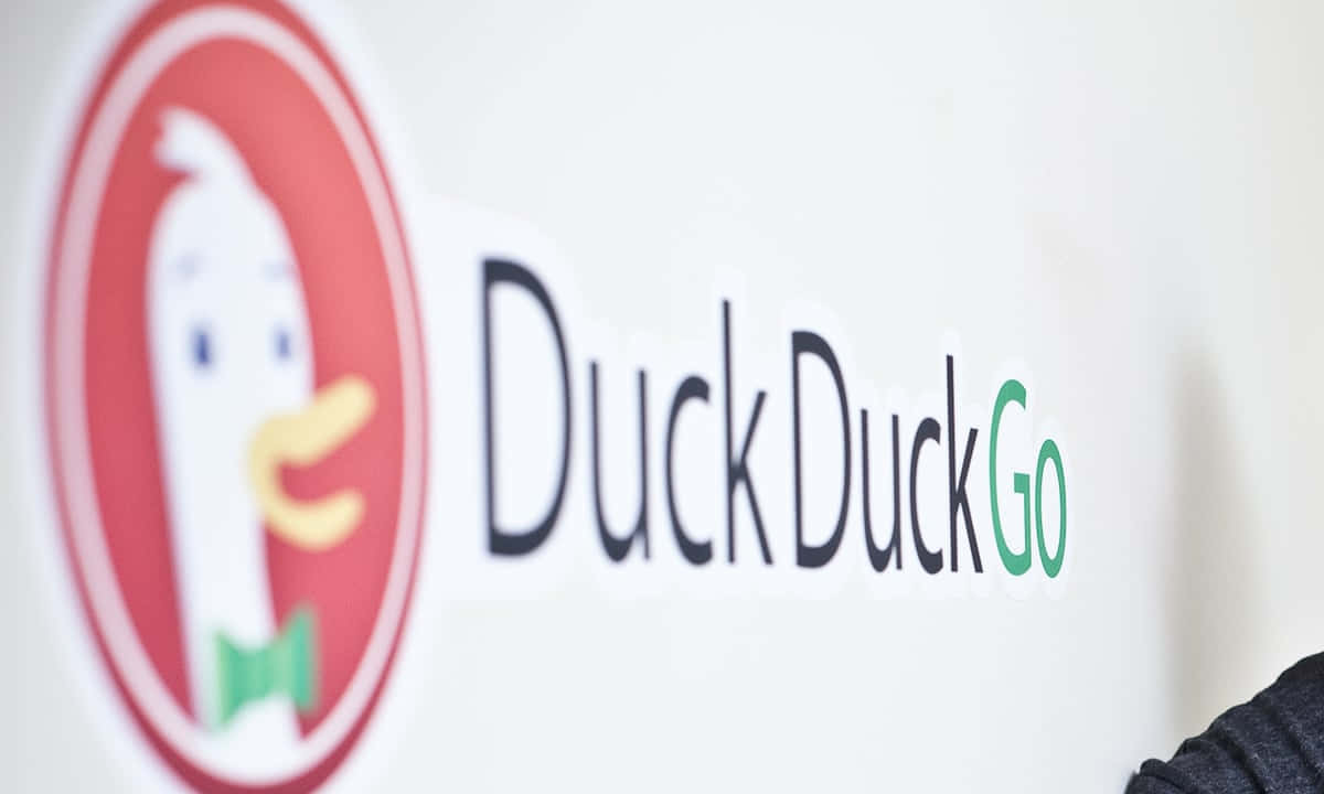 Duckduckgo 桌布 壁紙 — 白色牆上紅色圓圈內戴綠色蝴蝶結的卡通鴨 DuckDuckGo 標誌特寫。