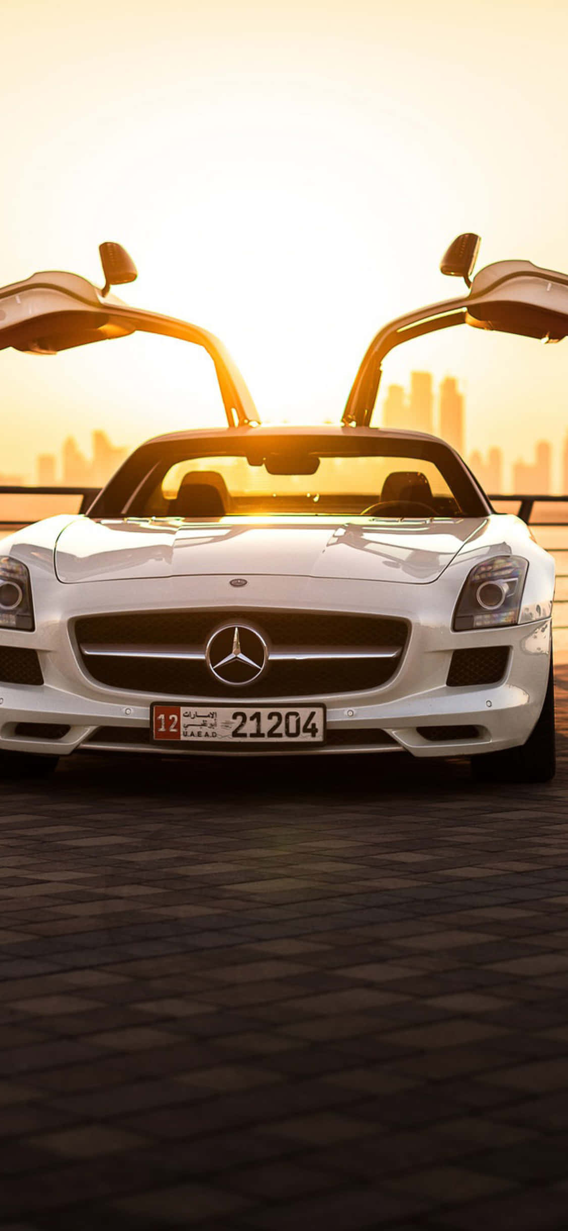 白色牛角門iPhone XS與梅賽德斯-AMG背景，SLS，陽光 壁紙 — 一架白色平治 SLS AMG 打開鷗翼車門，襯托著金色日落城市天際線。