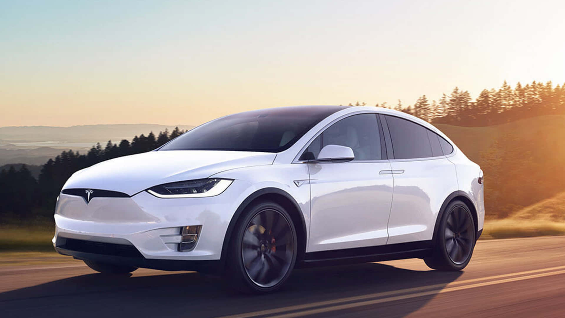 白色Tesla Model X在日落時分行駛在風景優美的道路上。