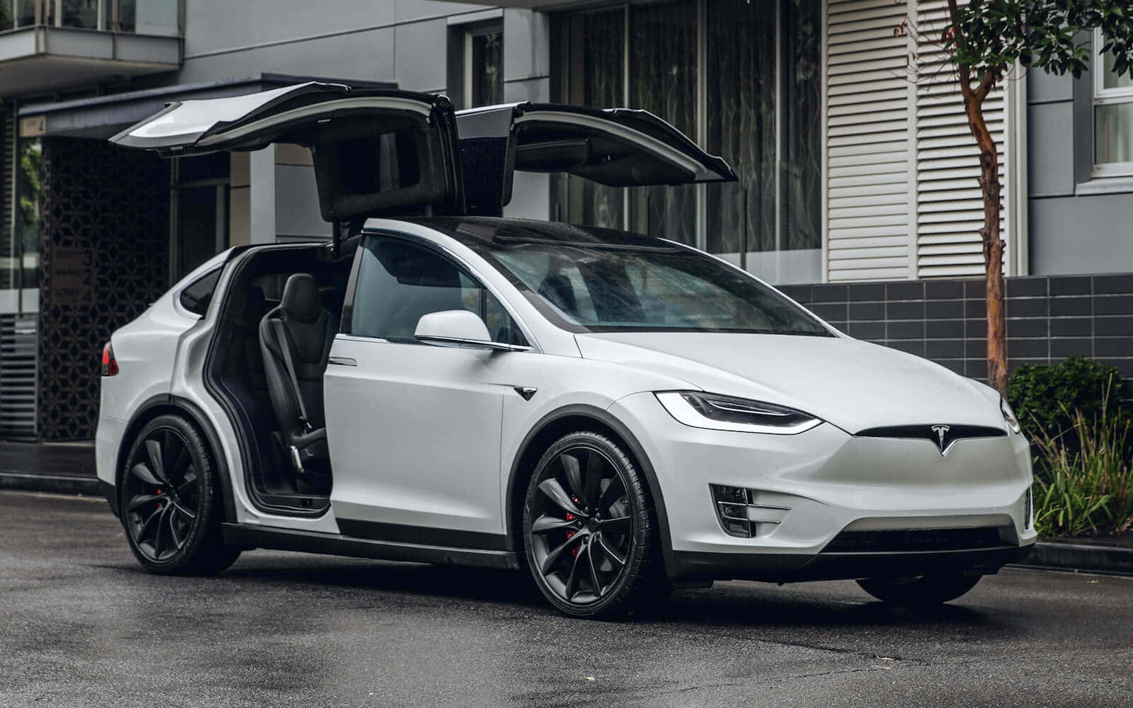 白色Tesla Model X，打開鷹翼門，停泊在濕潤街道上。