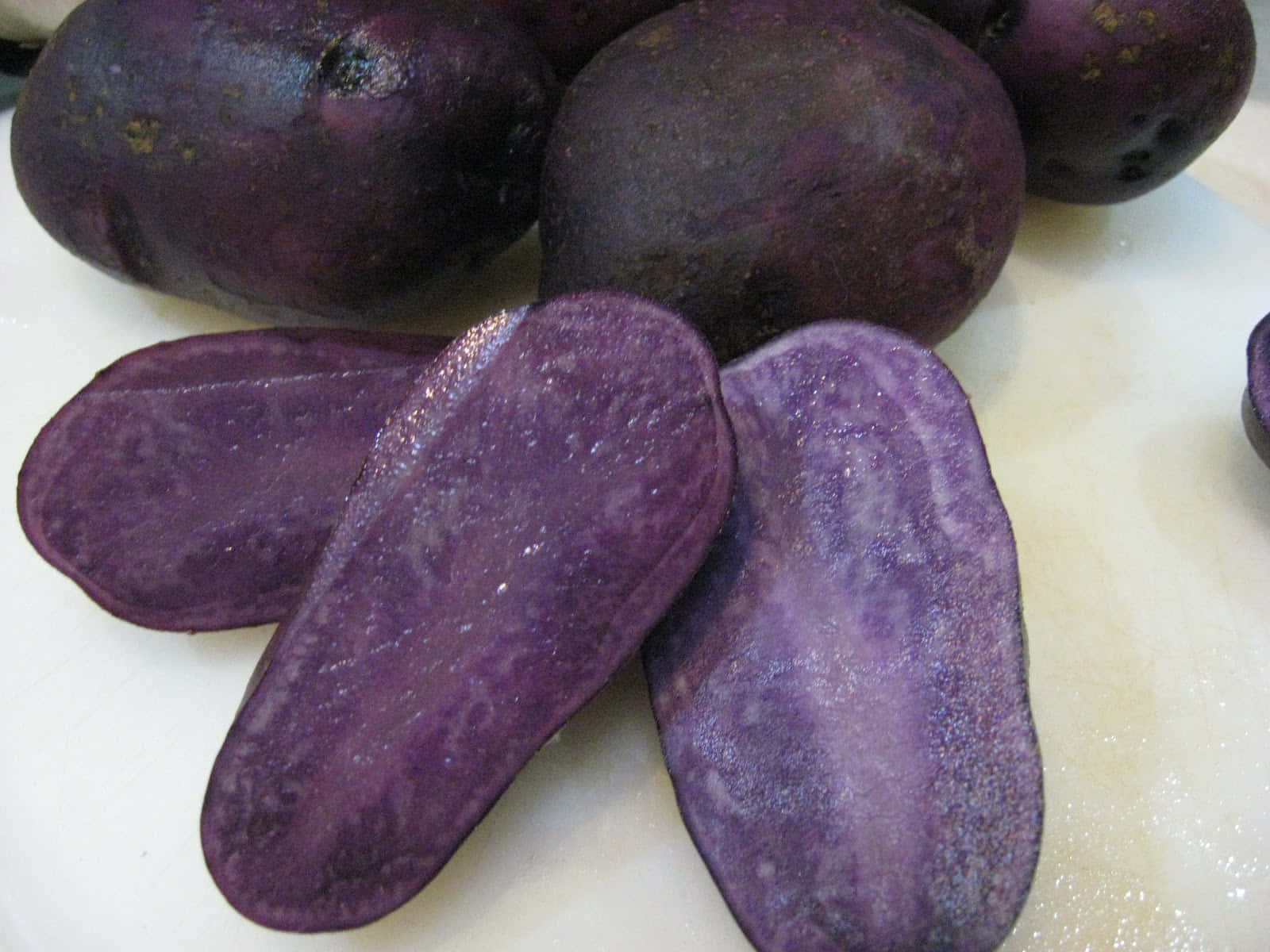Purple Potato 桌布 壁紙 — 白色砧板上鮮豔紫色馬鈴薯的特寫，切半露出深紫色果肉。