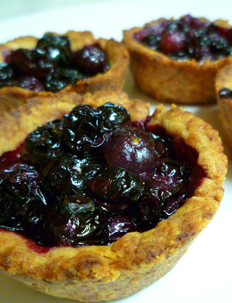 Blueberries Tart 桌布 壁紙 — 白色碟上擺放著金棕色外皮、光澤亮麗的藍莓撻特寫。