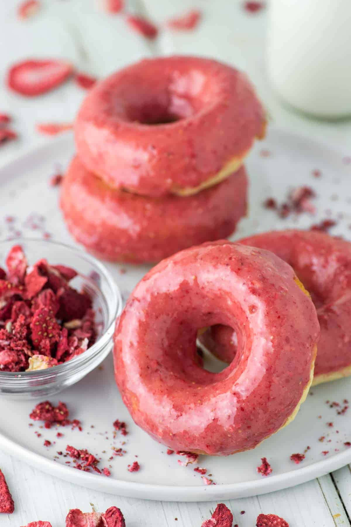 Glazed Donut 桌布 壁紙 — 白色碟上放著一堆粉紅色糖霜冬甩，上面有士多啤梨脆粒，旁邊有一杯牛奶。