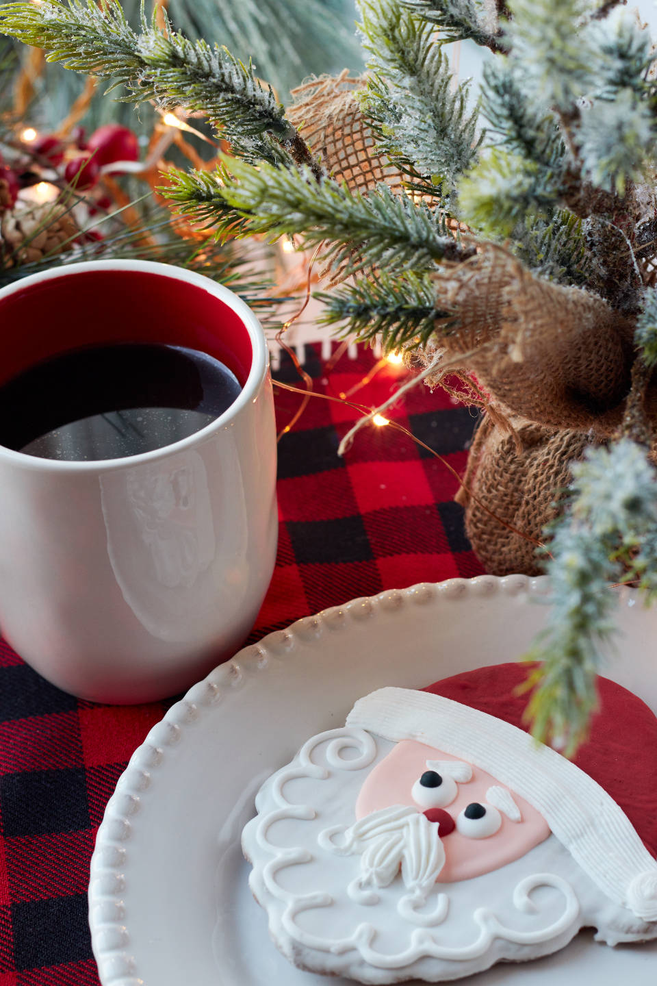 Santa Claus 桌布 壁紙 — 白色碟上的聖誕老人曲奇、紅色馬克杯、雪松枝和閃爍燈光的節日特寫。
