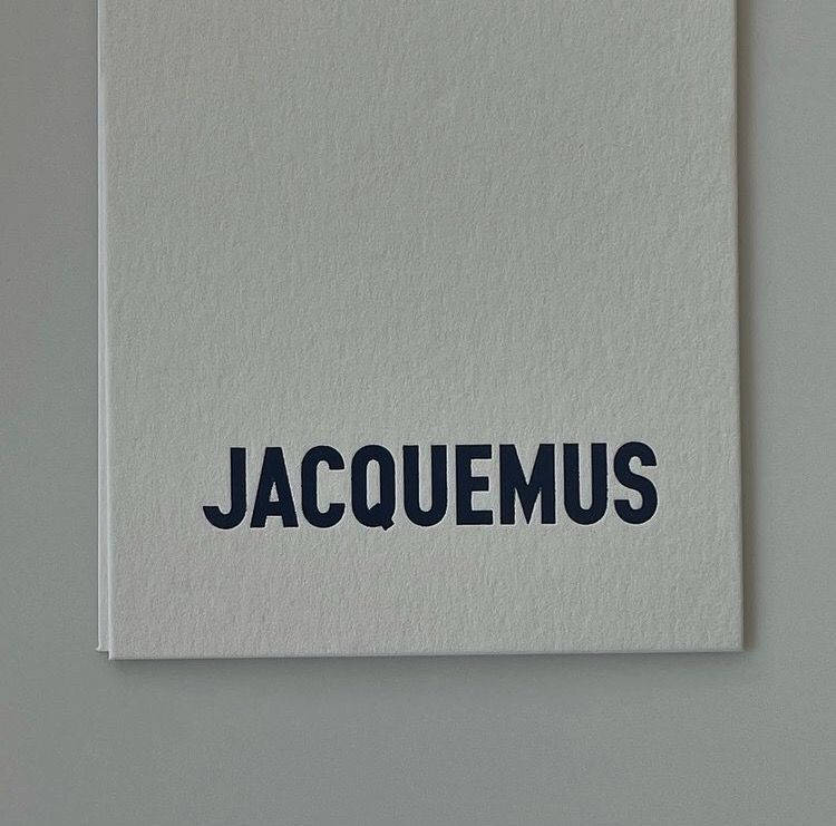 灰色紋理筆記本，帶有海軍藍色 JACQUEMUS 文字。