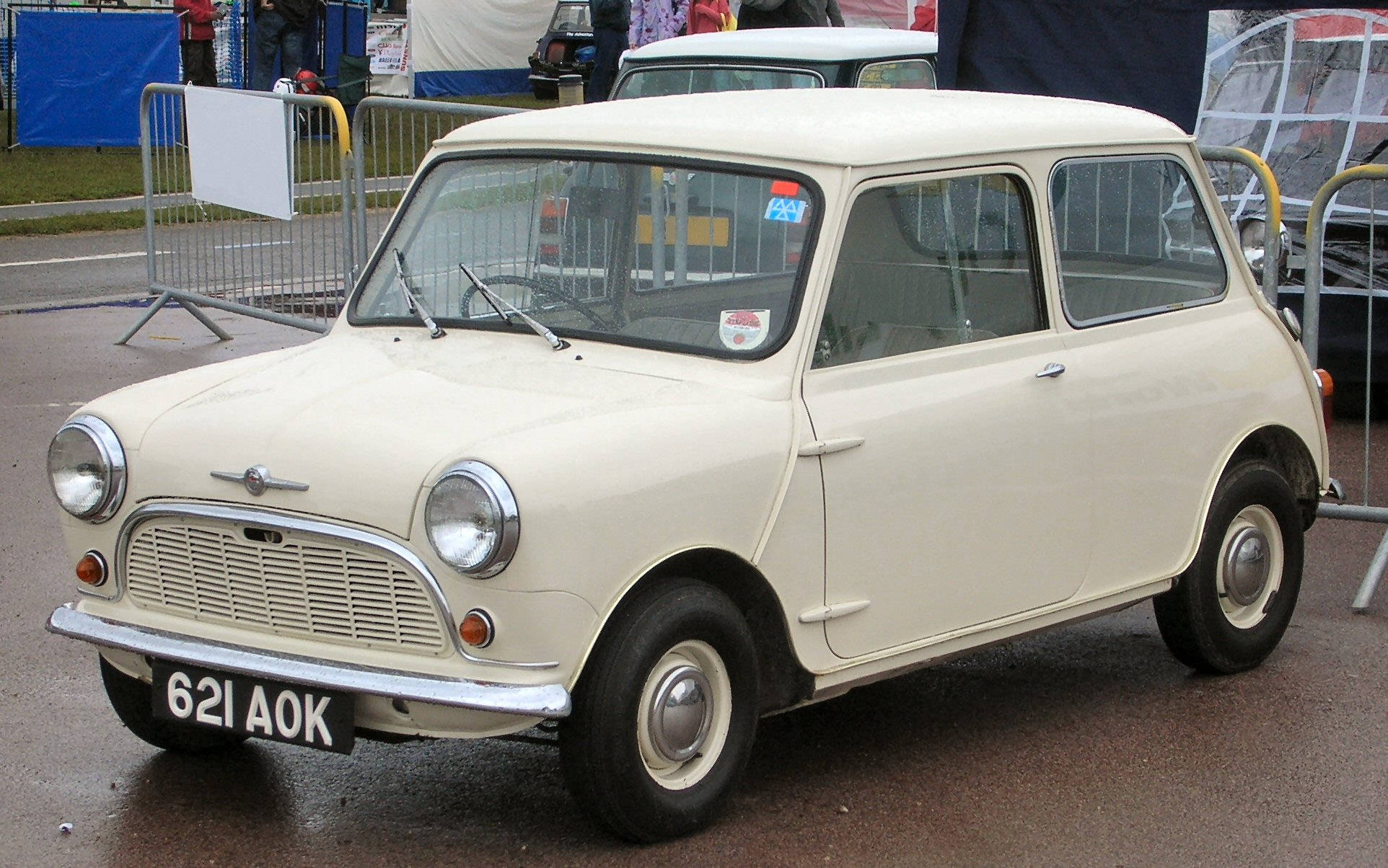 白色美學迷你車模型 壁紙 — 一輛復古奶油色Mini汽車，帶有鍍鉻裝飾，停在戶外活動的潮濕路面上。