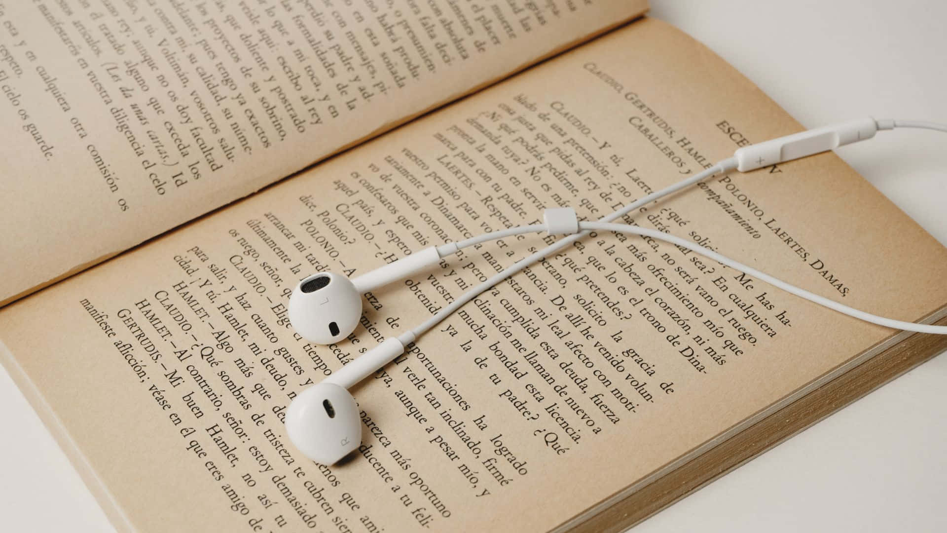 音樂美學 桌布 壁紙 — 白色耳機放在打開的書頁上，書頁有西班牙文文字，柔和自然光線。