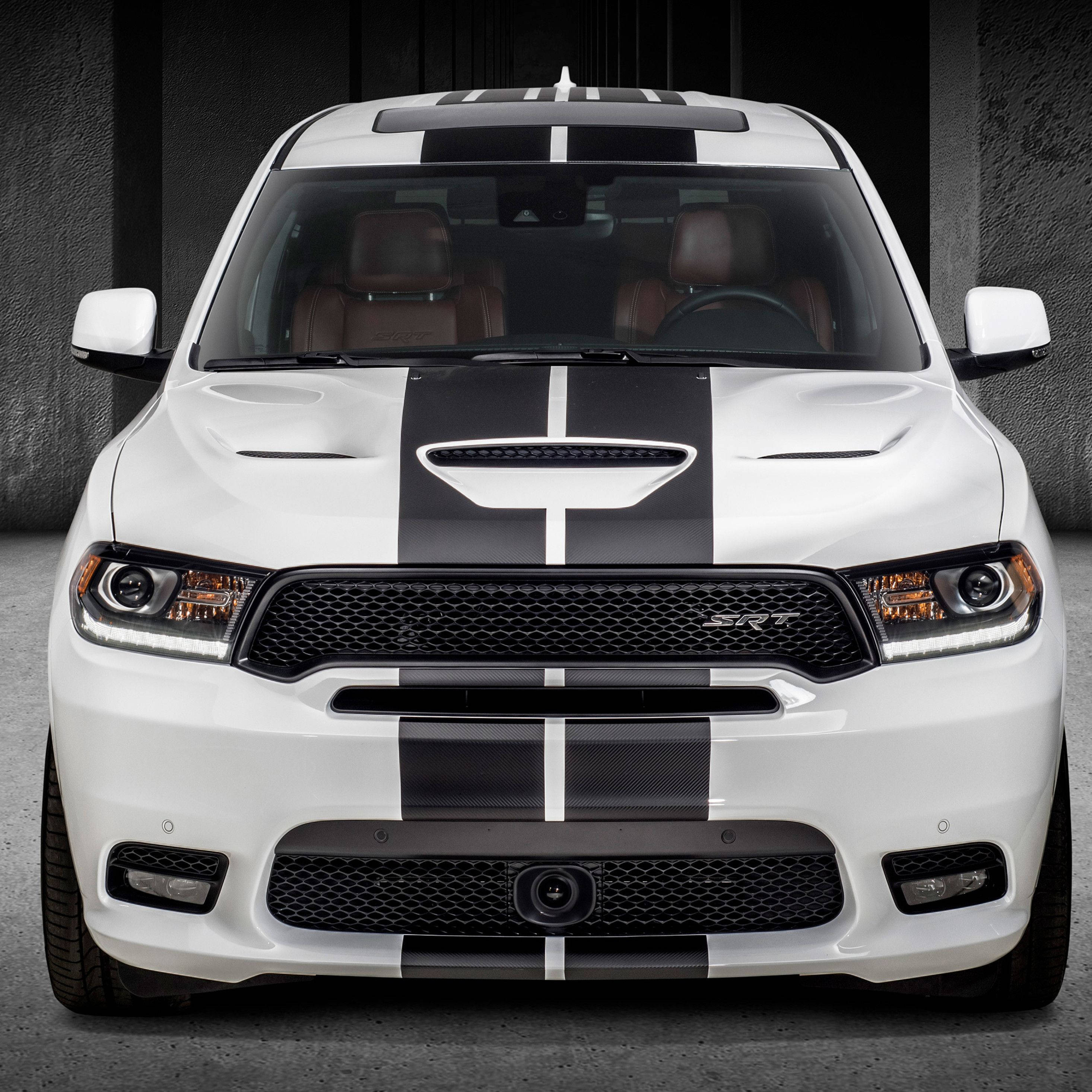 白色與黑色杜蘭戈細節前視 壁紙 — 一輛白色 Dodge Durango SRT 帶有醒目的黑色賽車條紋，在昏暗的工業車庫中向前凝視。