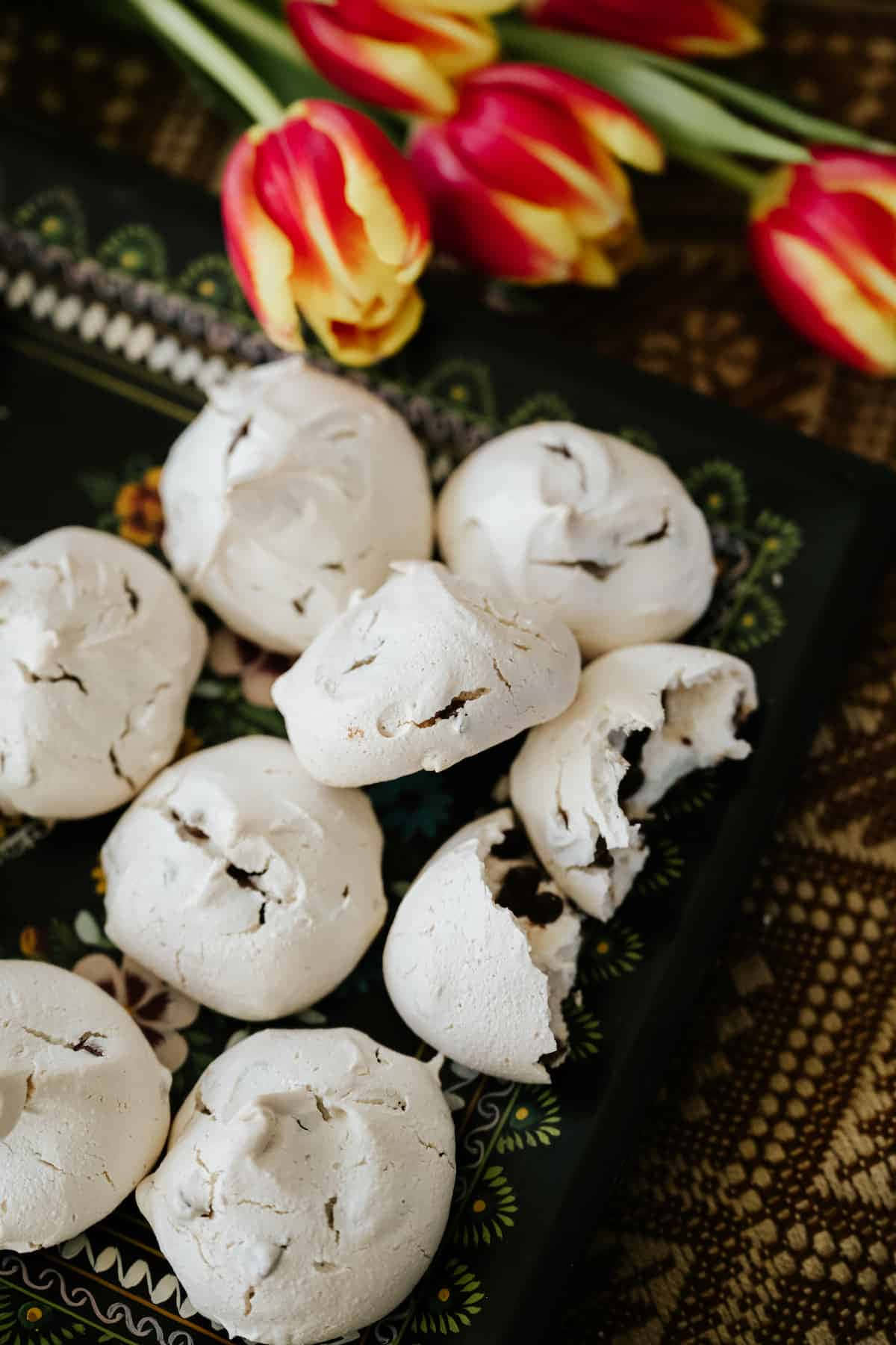 Meringue 桌布 壁紙 — 白色蛋白餅乾配黑朱古力粒，放在有圖案的黑色碟子上，旁邊有紅色和黃色鬱金香。
