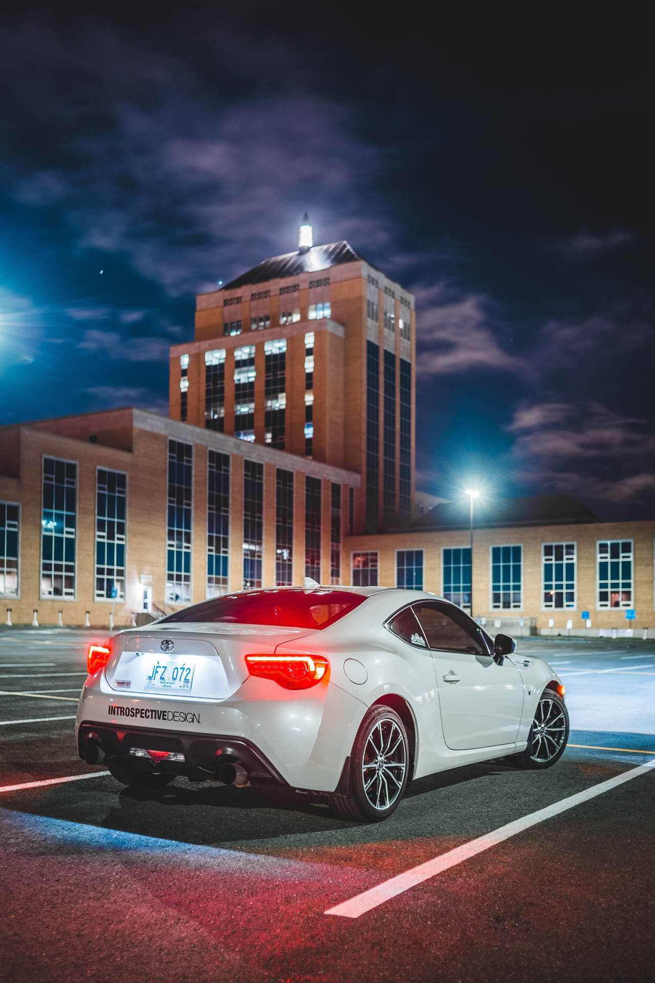 白色跑車在夜間停在明亮的城市建築前。