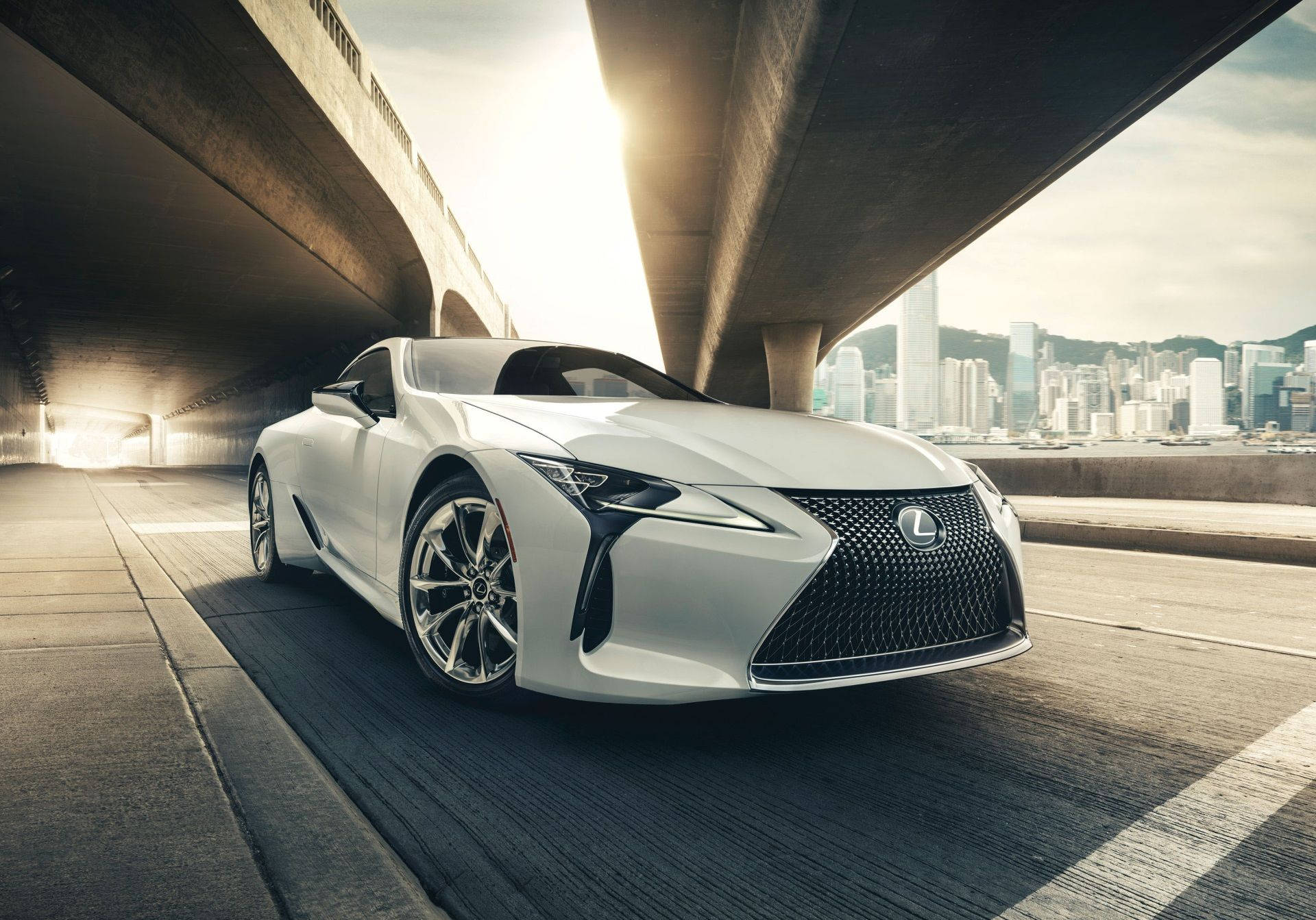 白色Lexus跑車在日落時分於城市高架橋下行駛。
