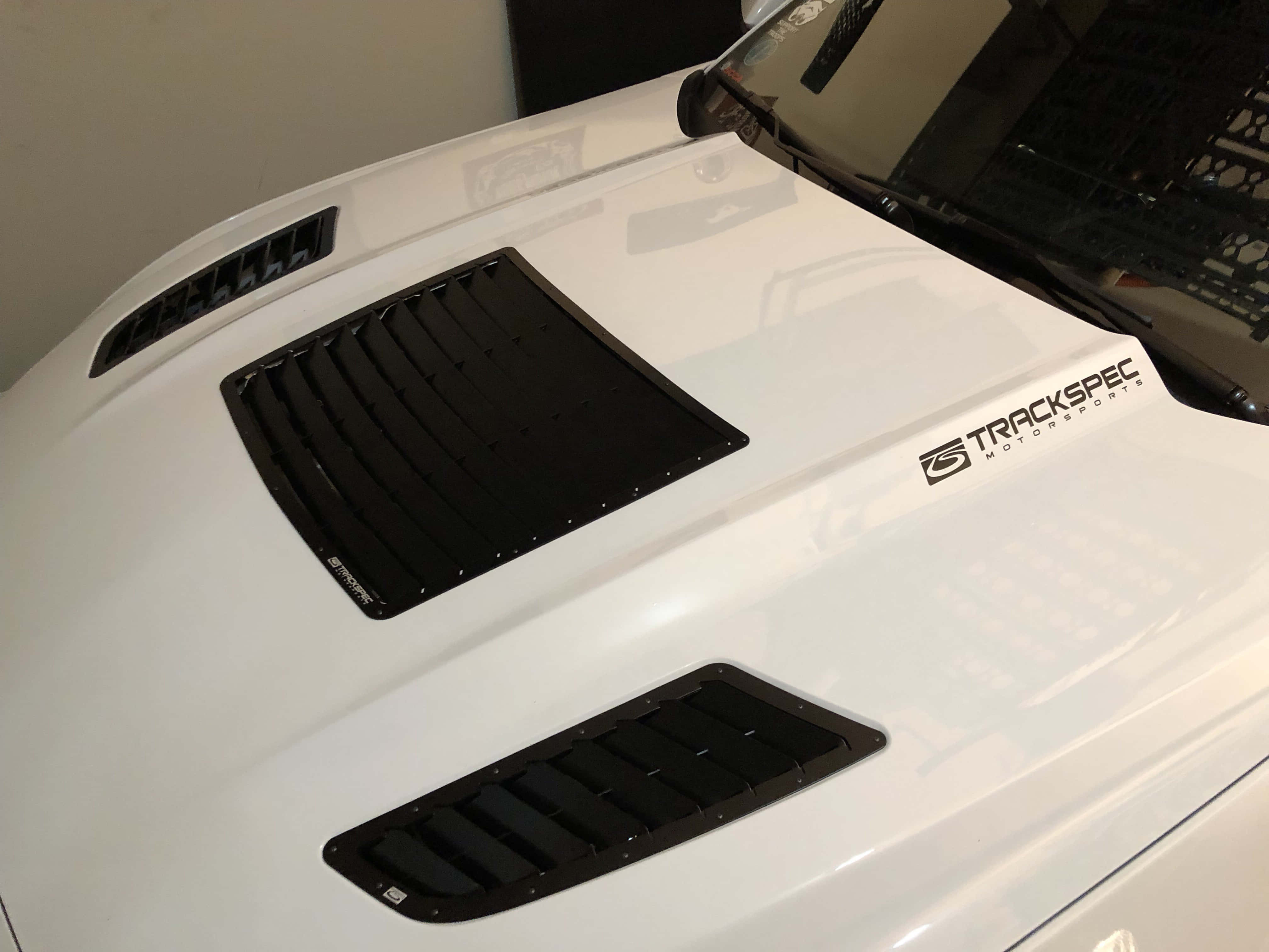 Car Hood 桌布 壁紙 — 白色跑車引擎蓋特寫，帶有黑色通風口和Trackspec Motorsports標誌。