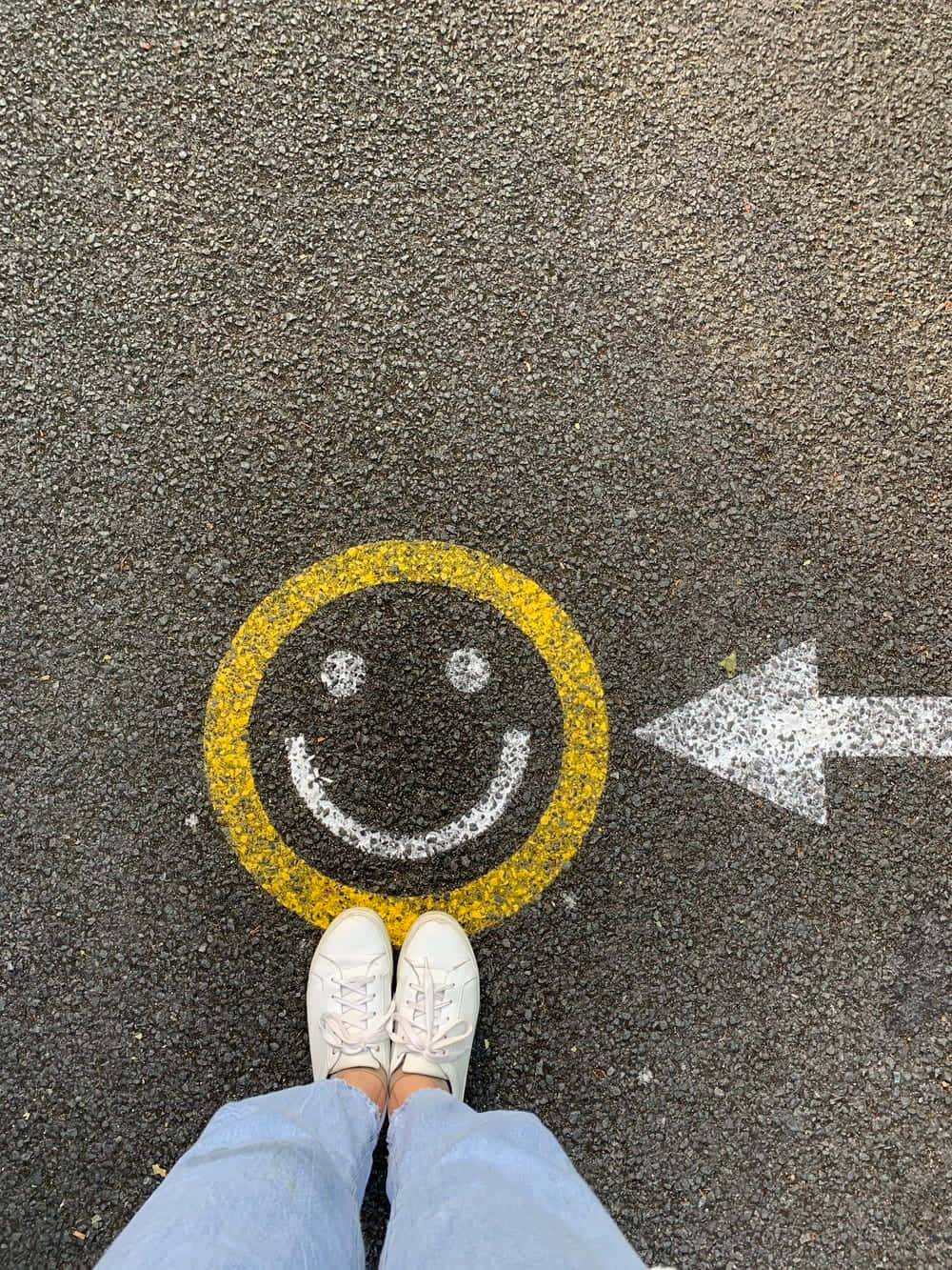 Aesthetic Smiley Face 桌布 壁紙 — 白色運動鞋企喺瀝青上面，旁邊有個黃色笑面同白色箭嘴指向左邊。