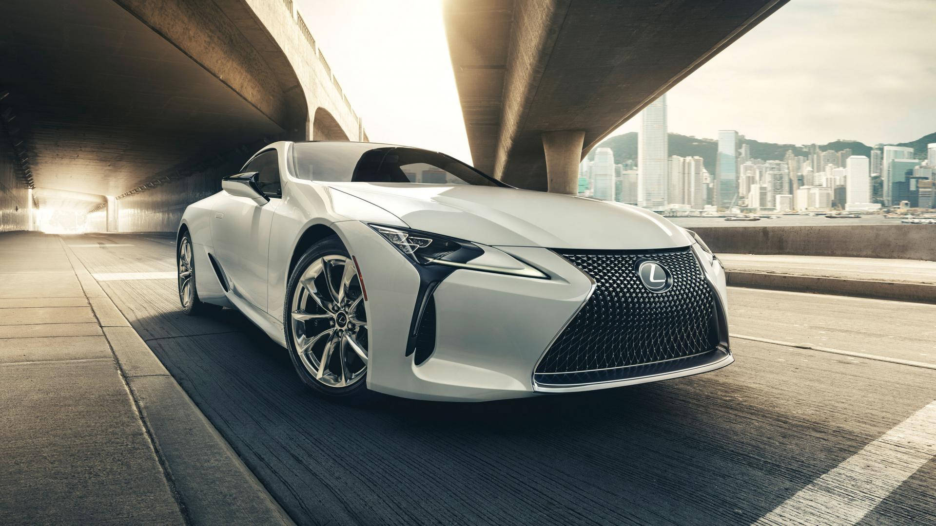 白色Lexus跑車在日落時分行駛於城市高架橋下。
