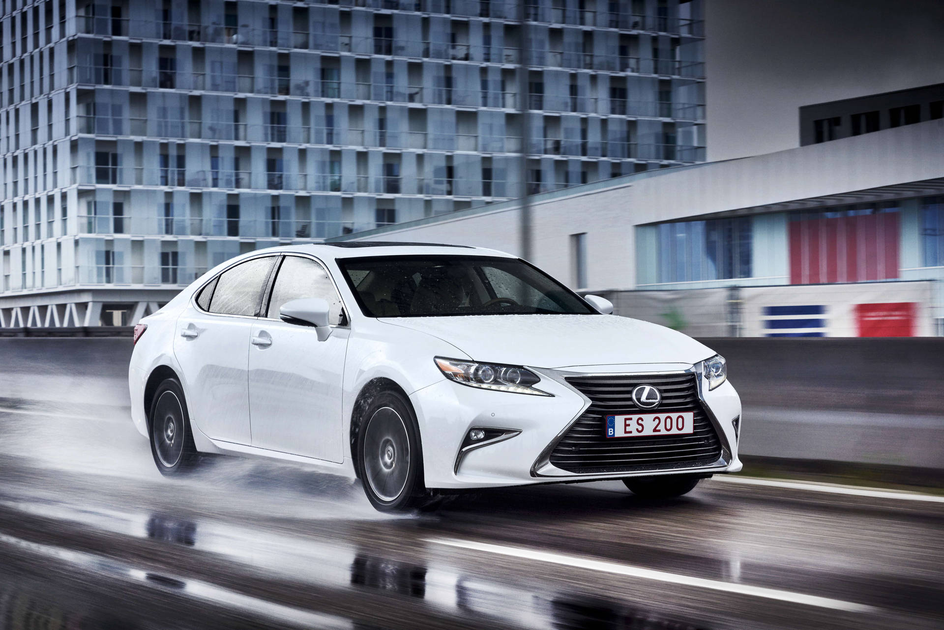 白色Lexus ES 200轎車在潮濕的城市街道上快速行駛，背景模糊。