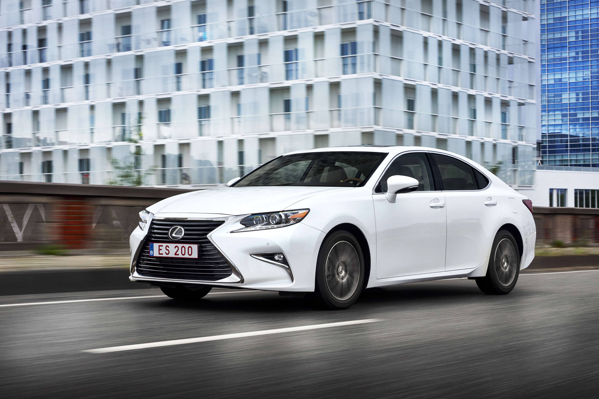 白色Lexus ES 200轎車在街道上行駛，背景是玻璃建築。