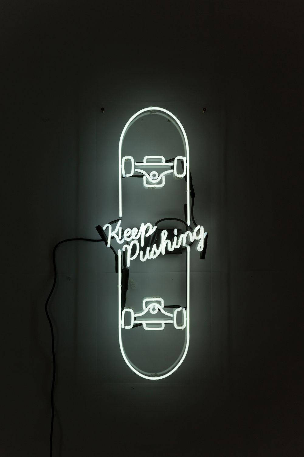 形狀像滑板的霓虹燈牌，上面有「Keep Pushing」的字樣，在黑暗的牆壁上發出白光。 — 滑板 壁紙