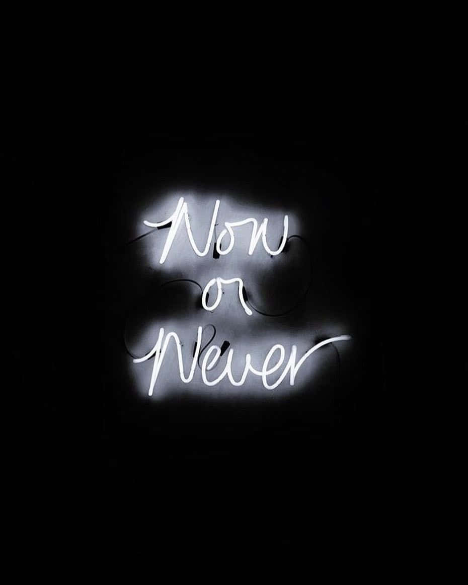 一個發光的霓虹燈牌，上面寫着「Now or Never」，在黑暗的房間裏。