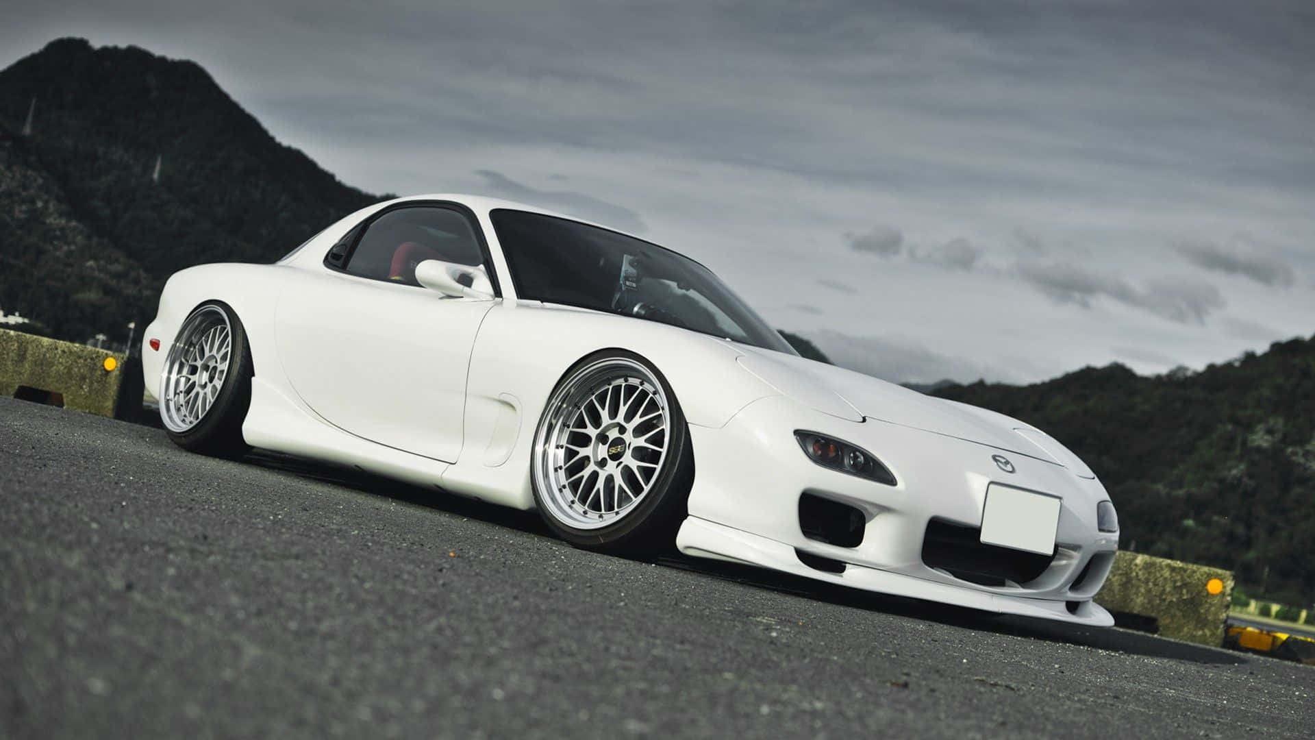 白色萬事得RX-7跑車停泊在山路上，背景為陰天天空。