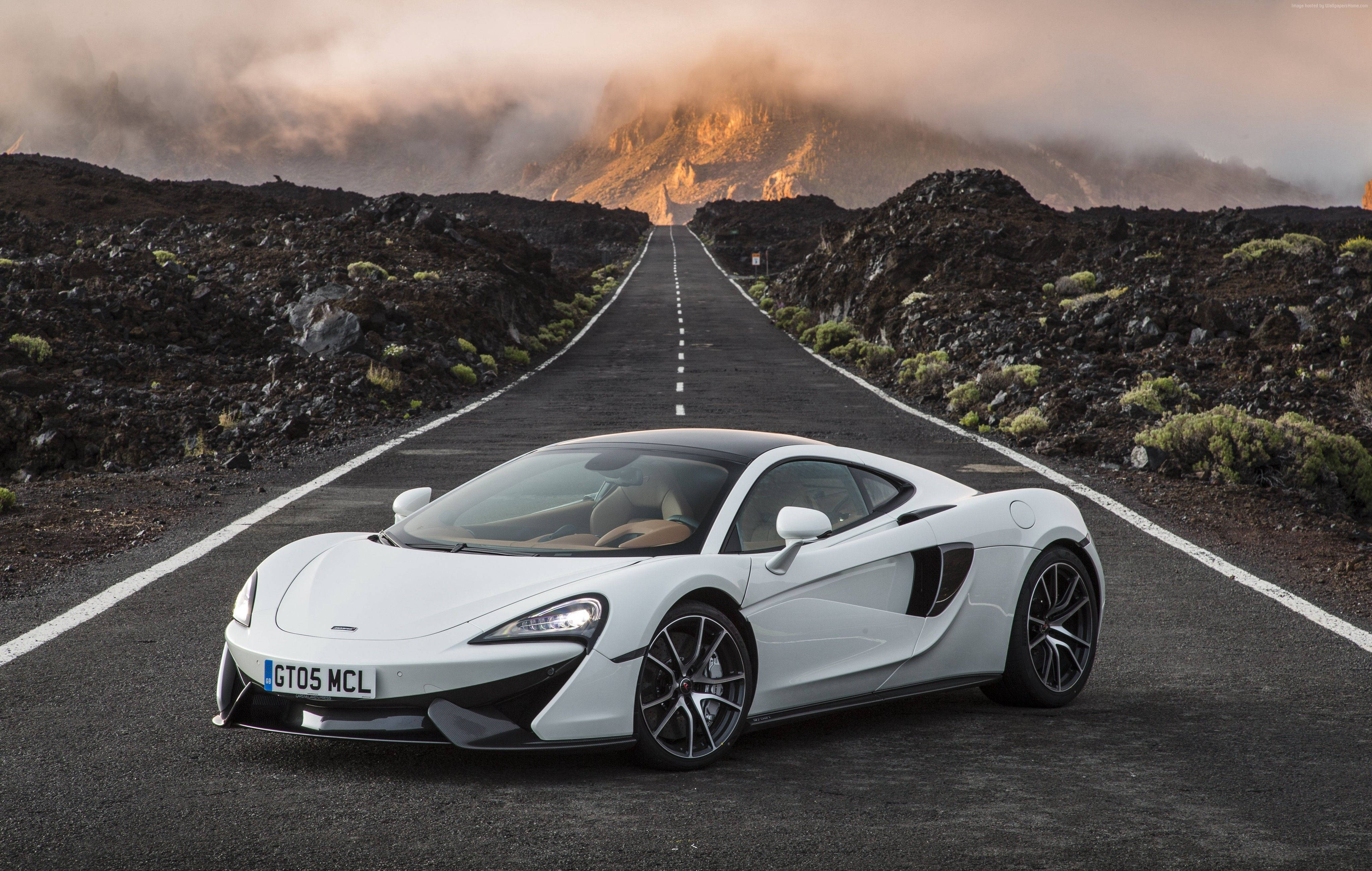白色麥拉倫570 GT 壁紙 — 一架流線型白色McLaren跑車在日落時分，停在一條穿越崎嶇火山景觀的直路上。