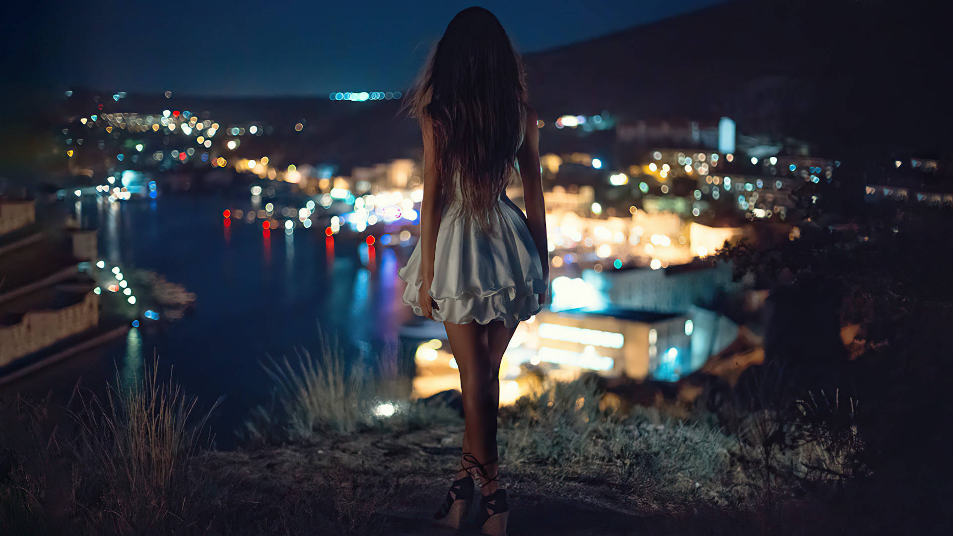身穿白色連衣裙的女子在夜晚俯瞰閃爍的沿海小鎮