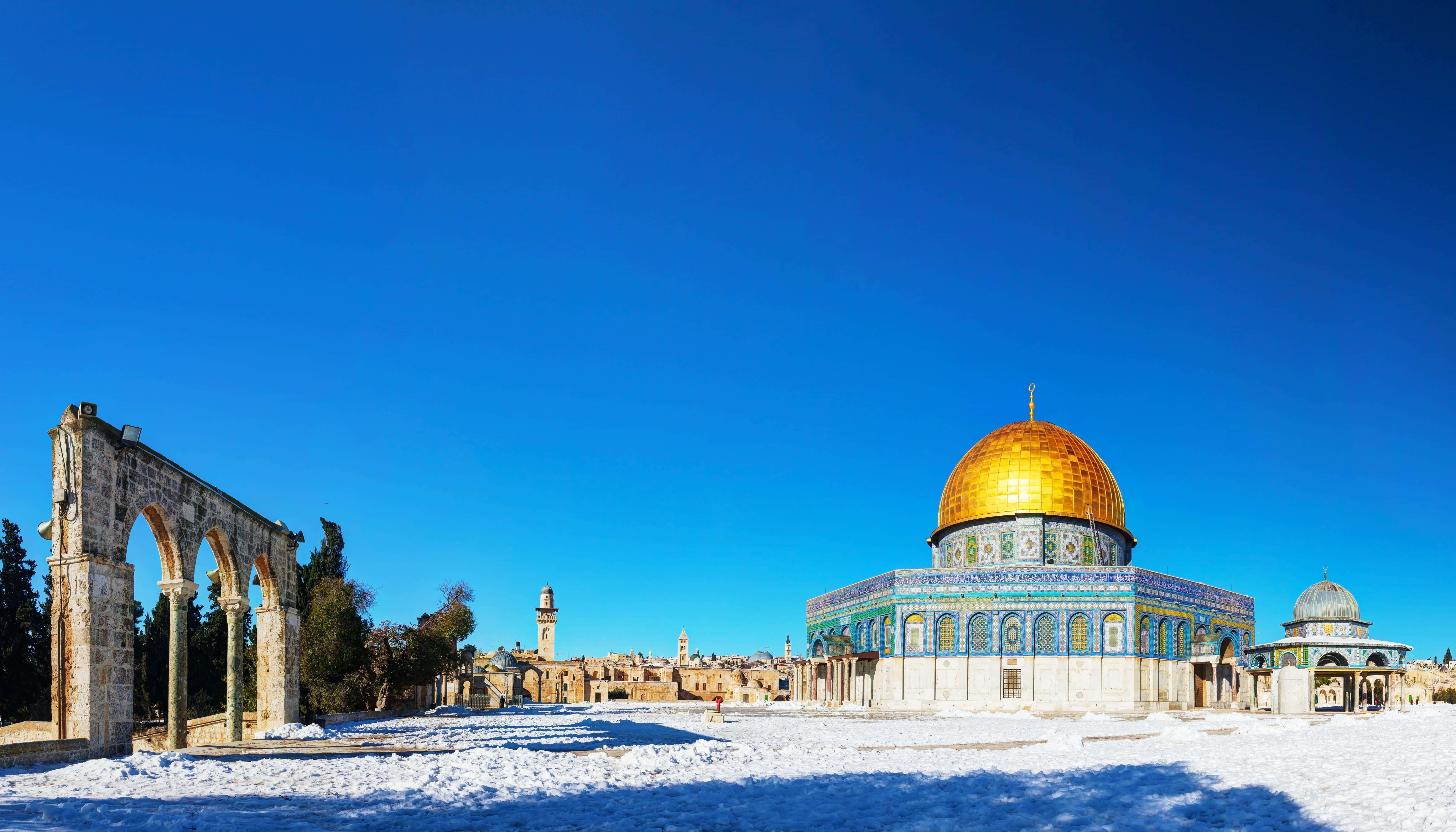 Israel 桌布 壁紙 — 白雪覆蓋地面，左邊有古老石拱門，金色圓頂清真寺在清澈藍天下矗立。