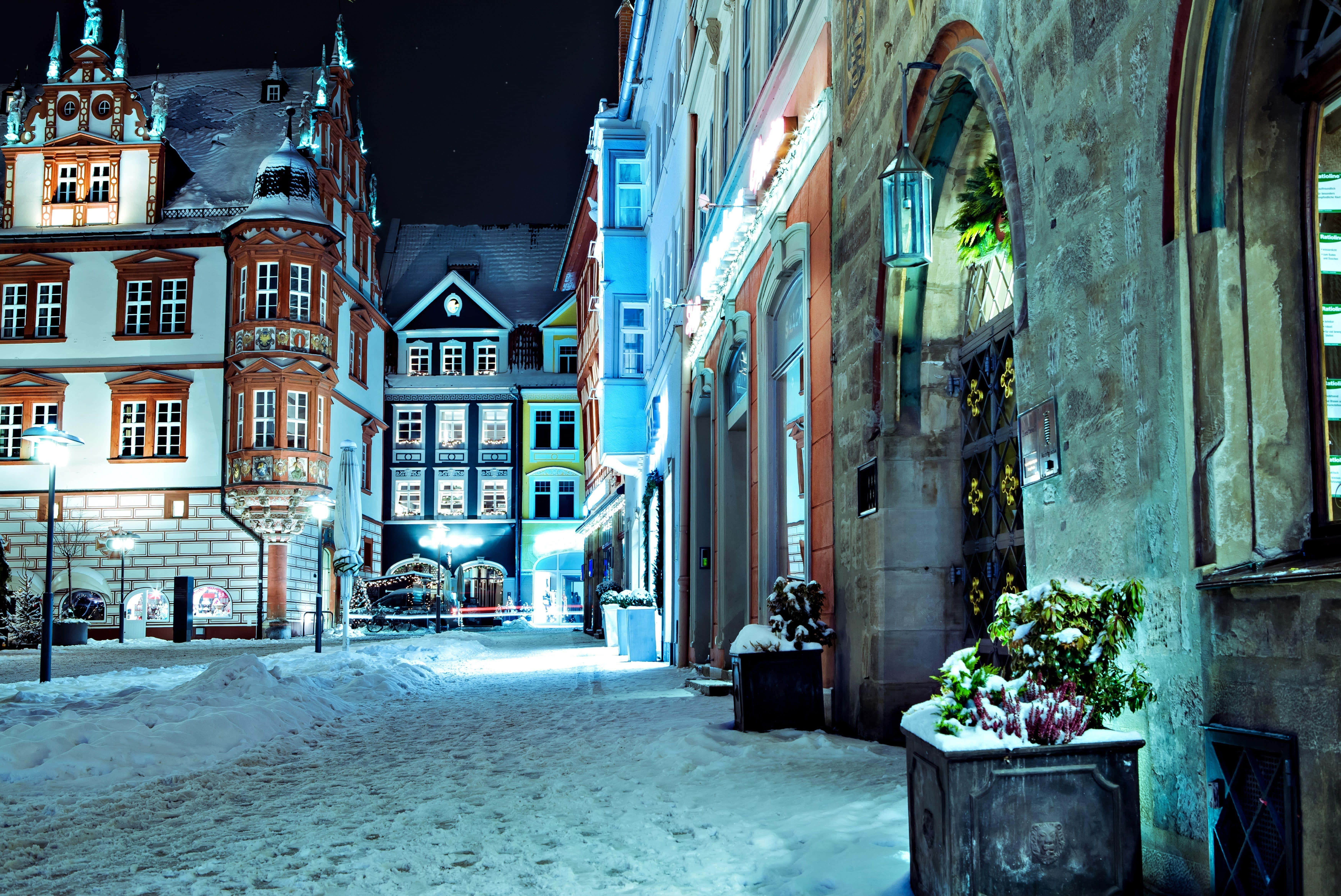 Germany 桌布 壁紙 — 白雪覆蓋夜晚狹窄的歐洲街道，溫暖的燈光從裝飾華麗的歷史建築中透出。