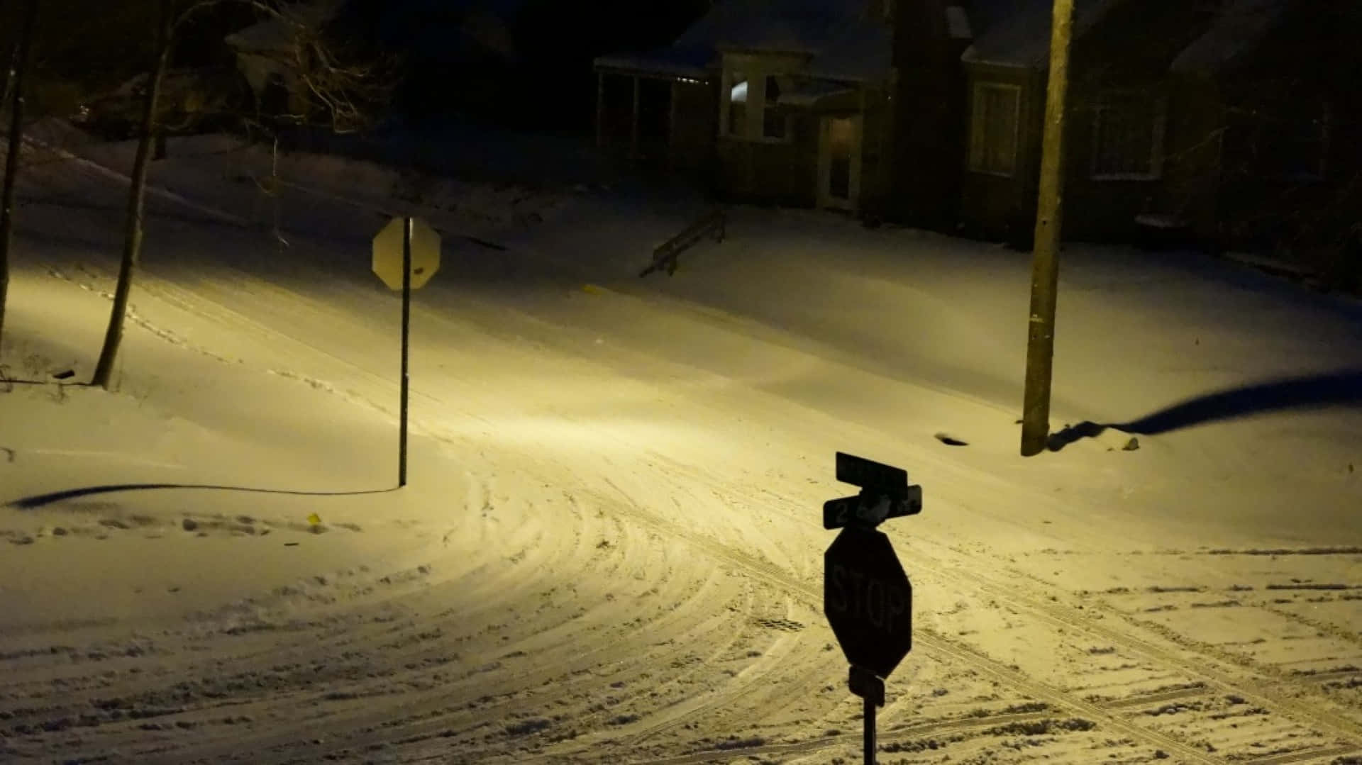 夜晚積雪的街道，路燈下有停車標誌和房屋。 — 寶麗來 GIF 壁紙